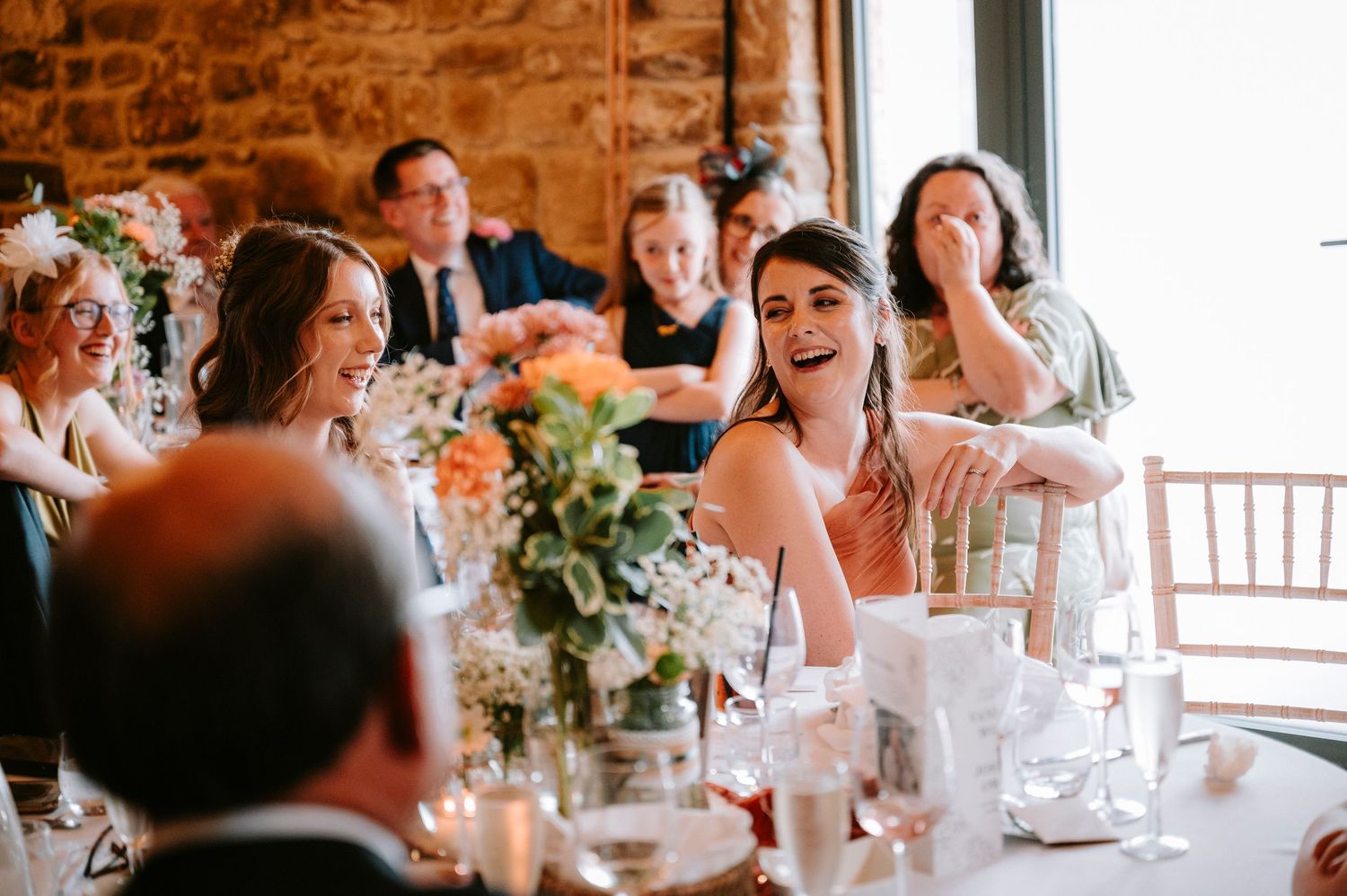 Wedding reception scene with guests dining and celebrating at decorated tables in a stone-walled venue.