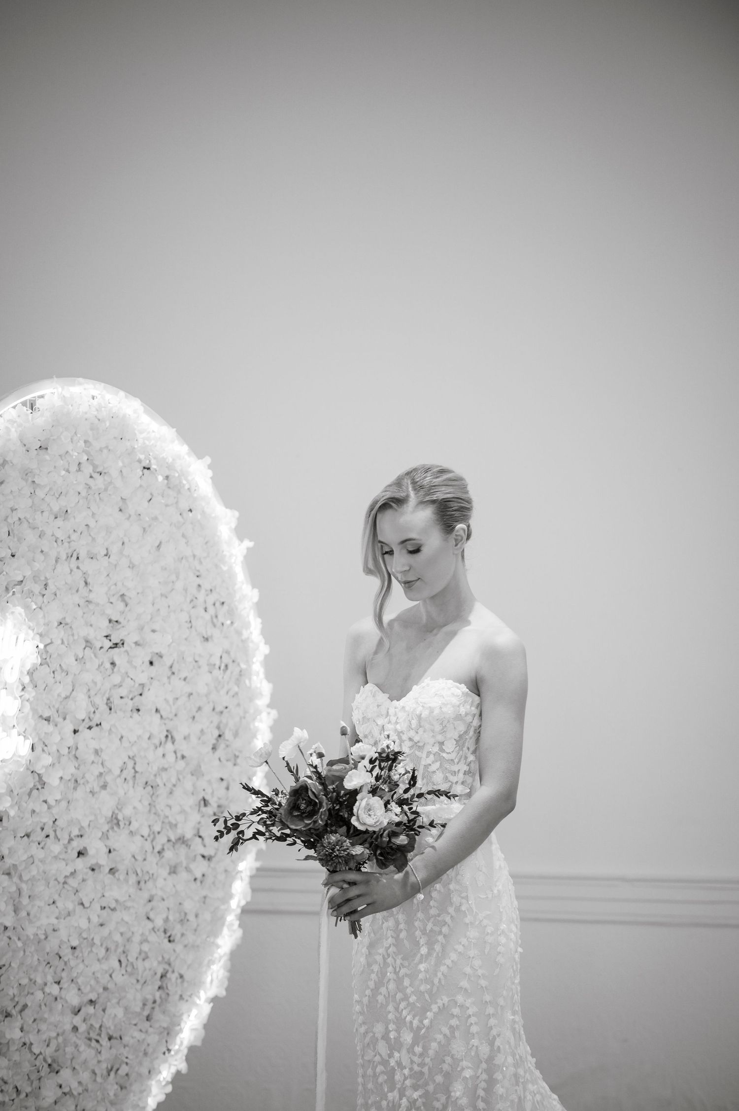 A black and white bridal portrait with a dramatic floral backdrop and bouquet.