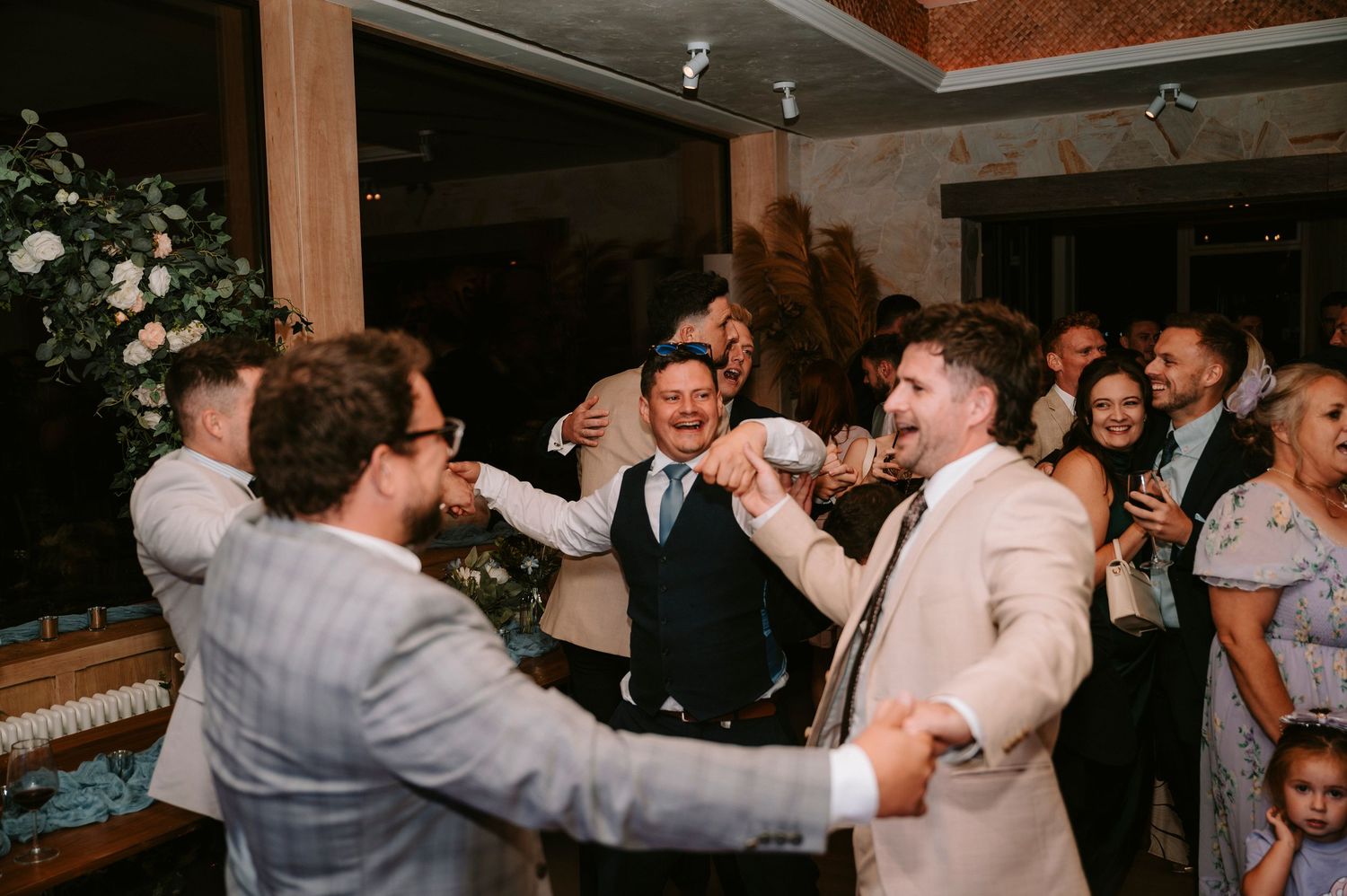 Wedding reception dance party with guests celebrating in a dimly lit venue.