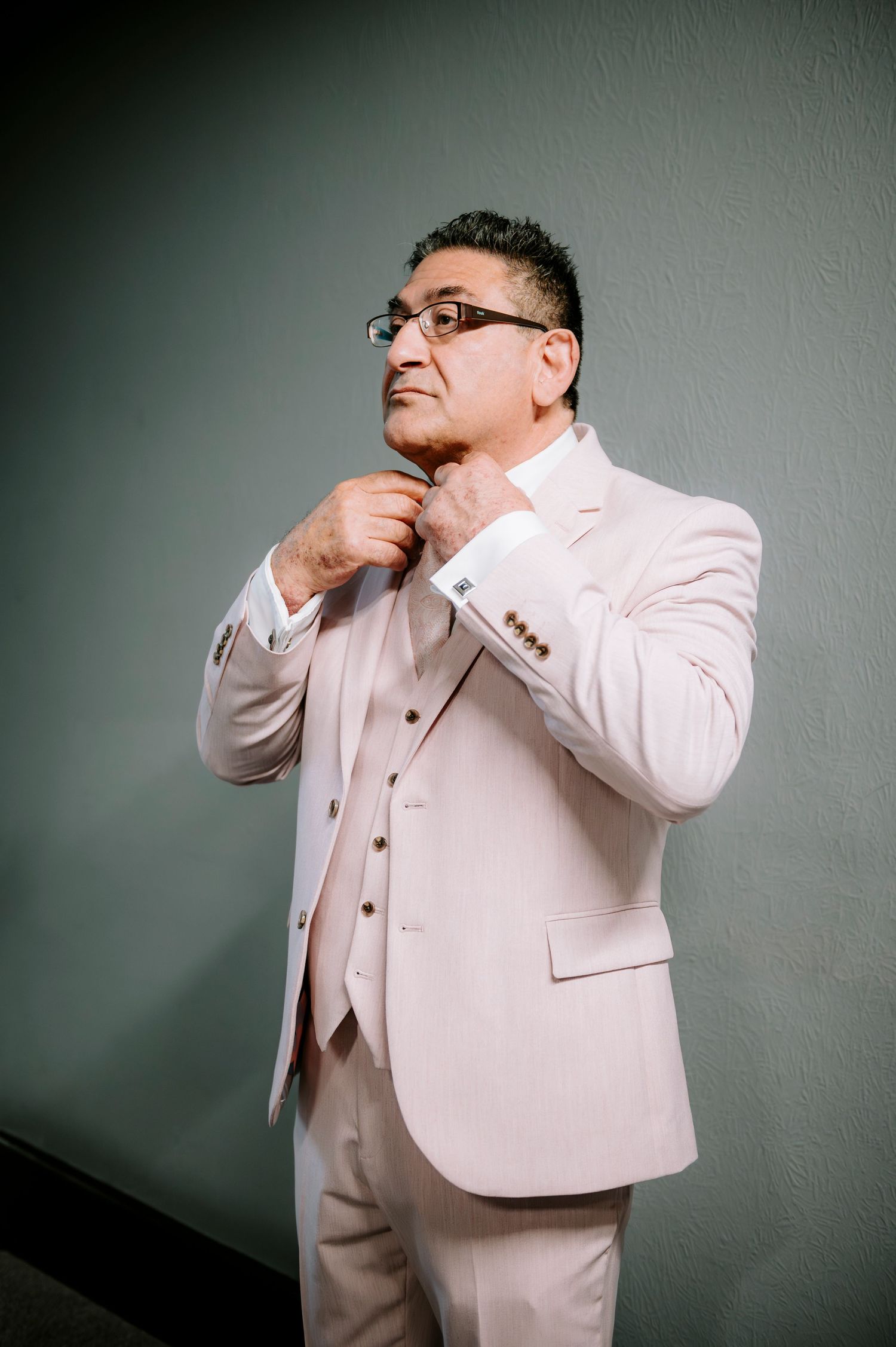Person in light colored formal suit making playful gestures against a gray wall.
