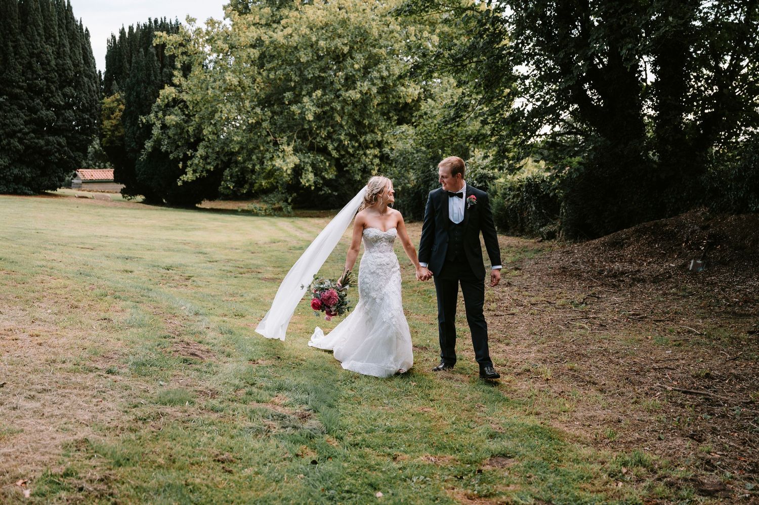 Newlyweds walk through garden setting during wedding photo session.