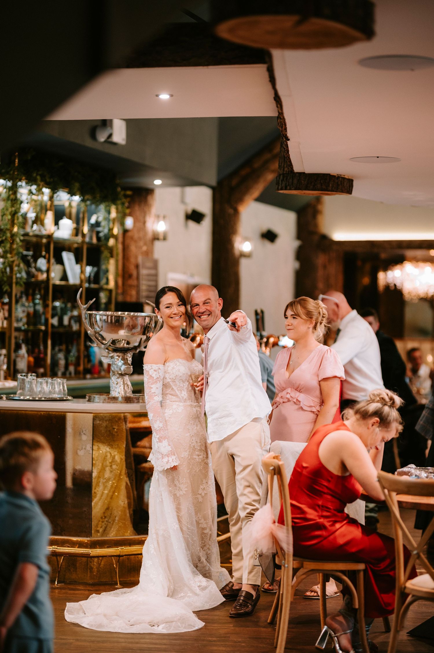 Newlyweds and guests celebrate near a rustic bar area with a large trophy displayed.