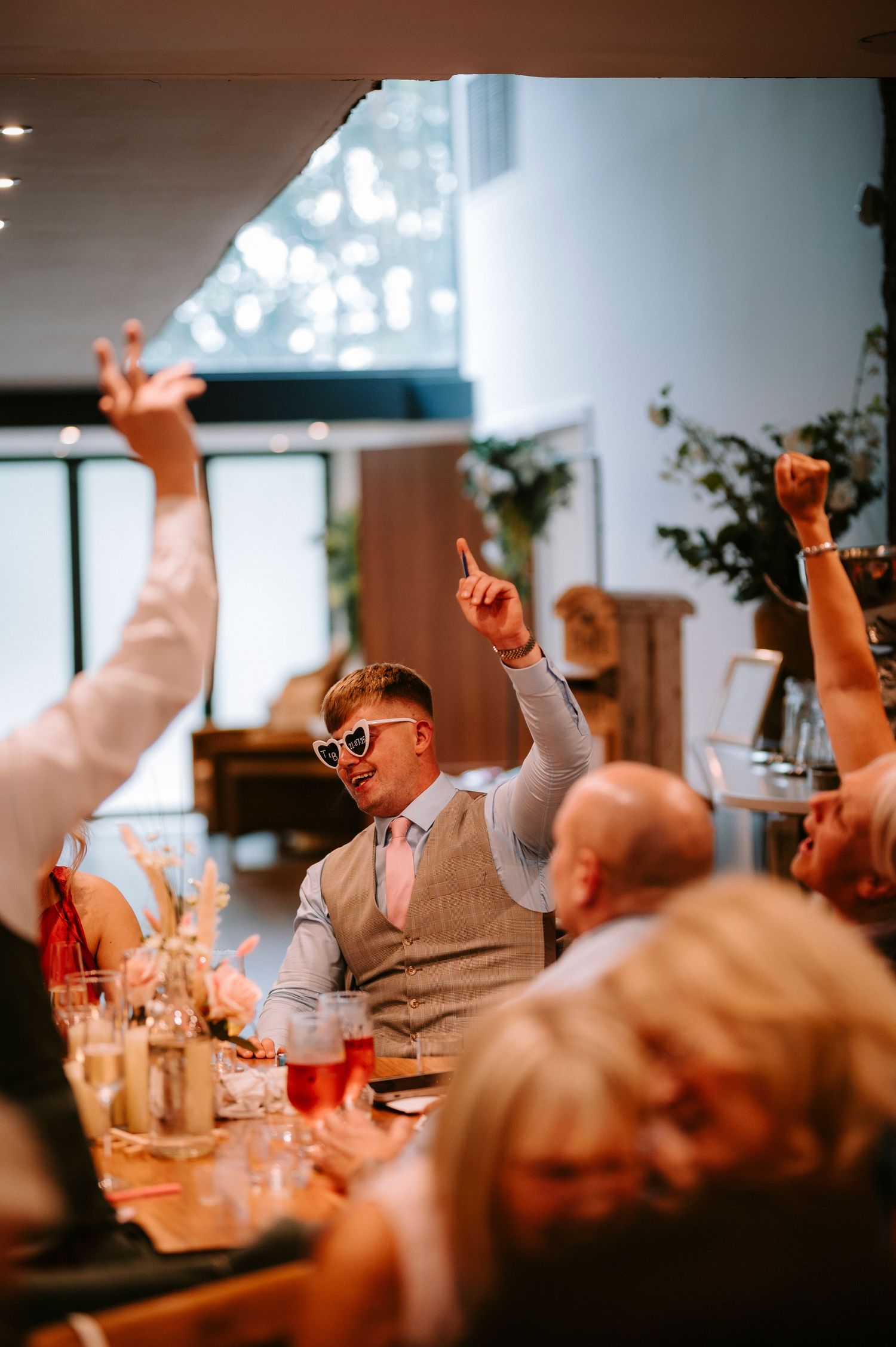 Wedding reception guests raise their hands in celebration during a festive dinner party.