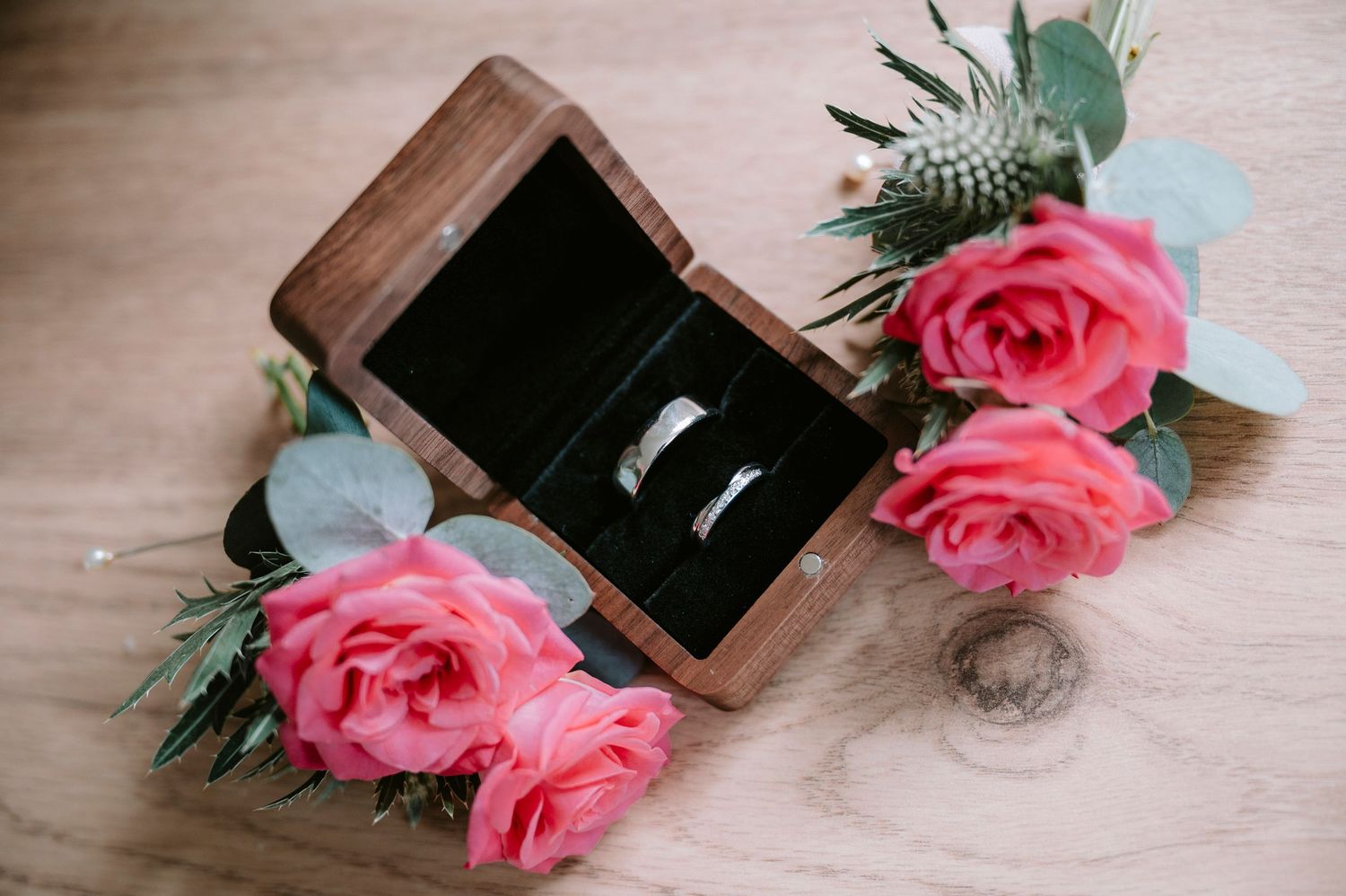 Pink roses and wooden ring box arranged on light wooden surface.