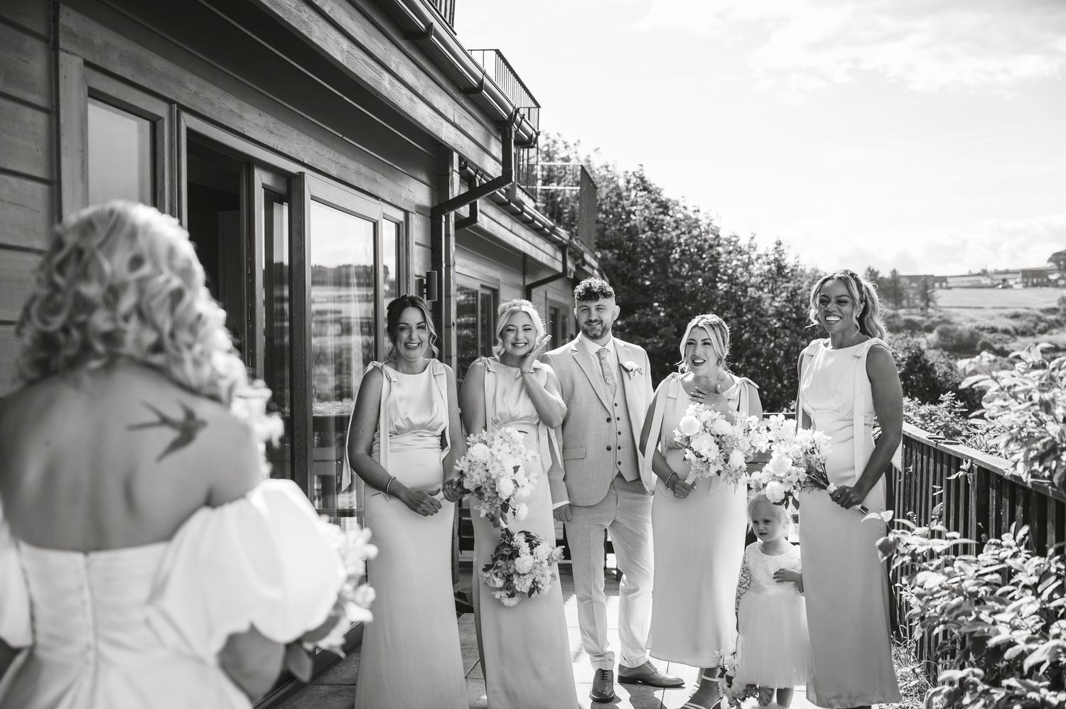 Black and white photo of bridal party gathered on outdoor deck during wedding celebration.