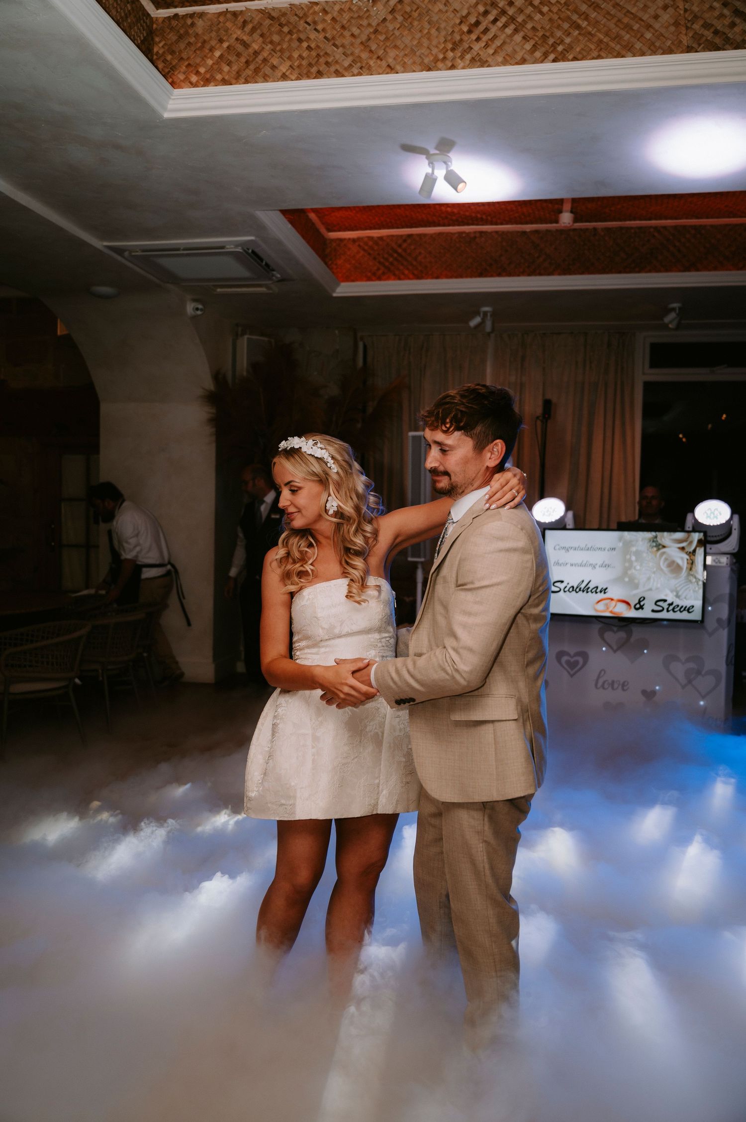 Newlyweds share a romantic dance surrounded by atmospheric fog effects on the dance floor.