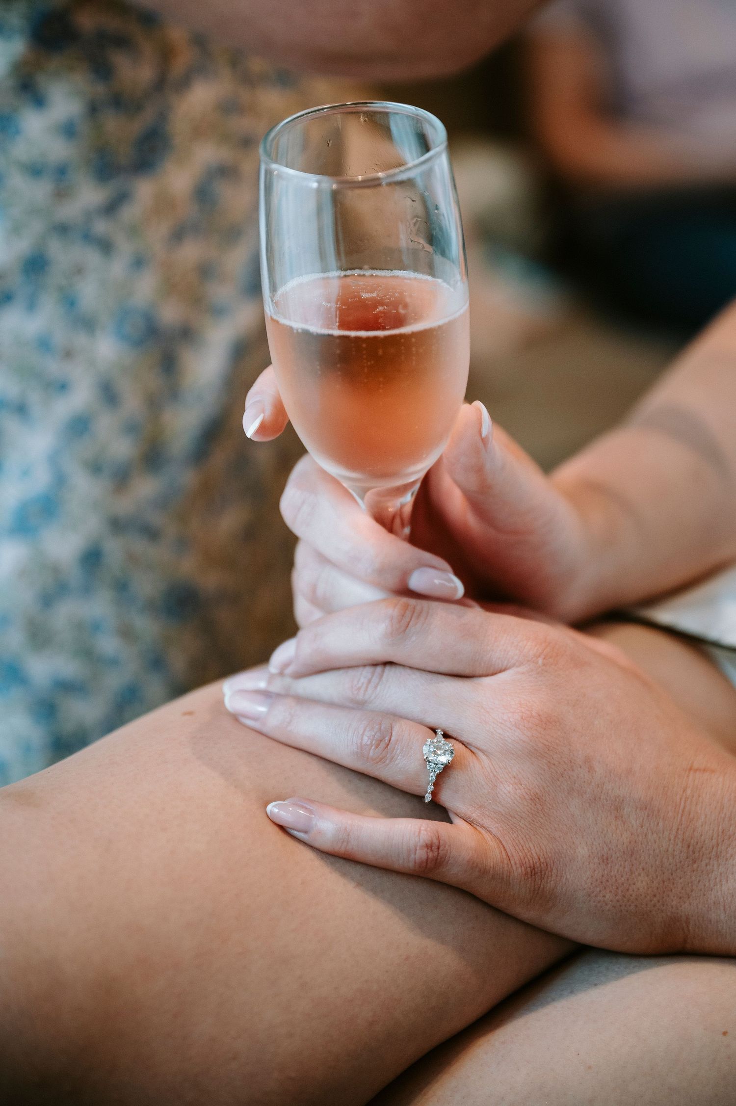 Hand holding glass of rose wine showing engagement ring detail.