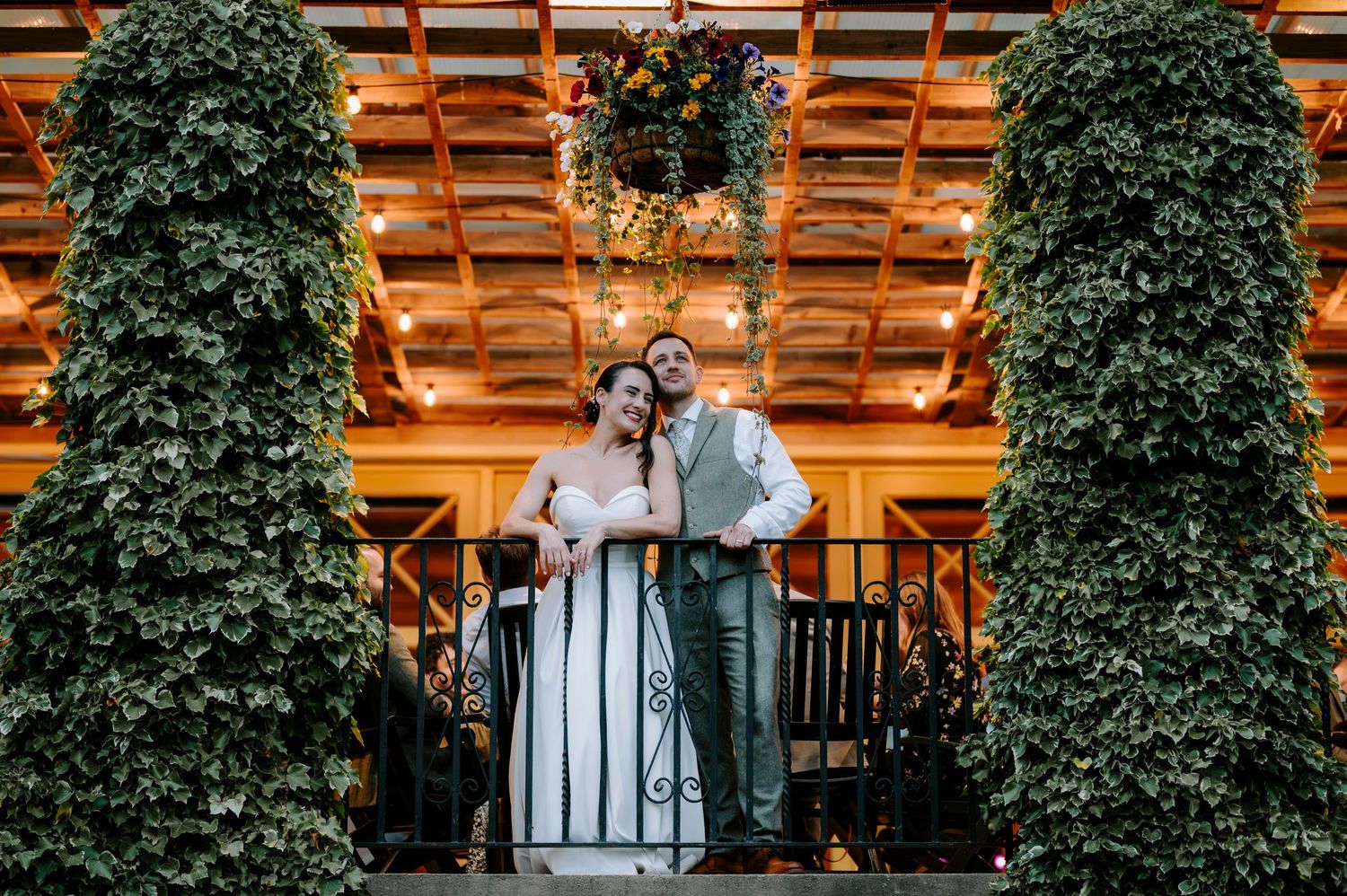 A romantic moment between newlyweds on a balcony with decorative greenery and warm lighting.