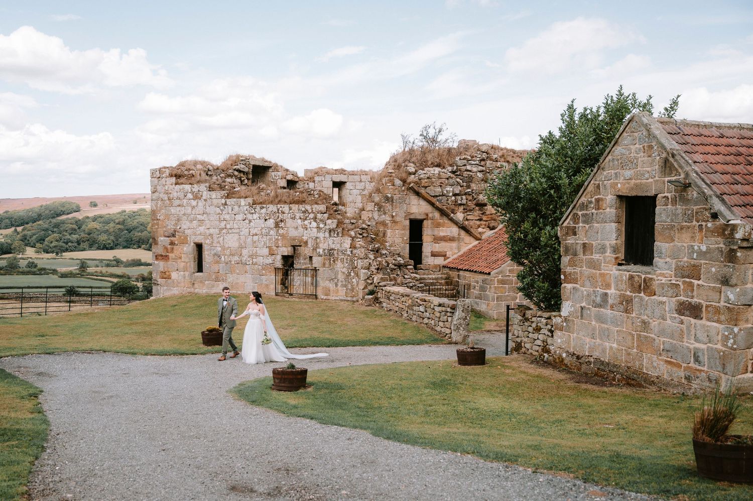 Stone ruins of a historic building stand against a scenic rural landscape with rolling hills in the background.