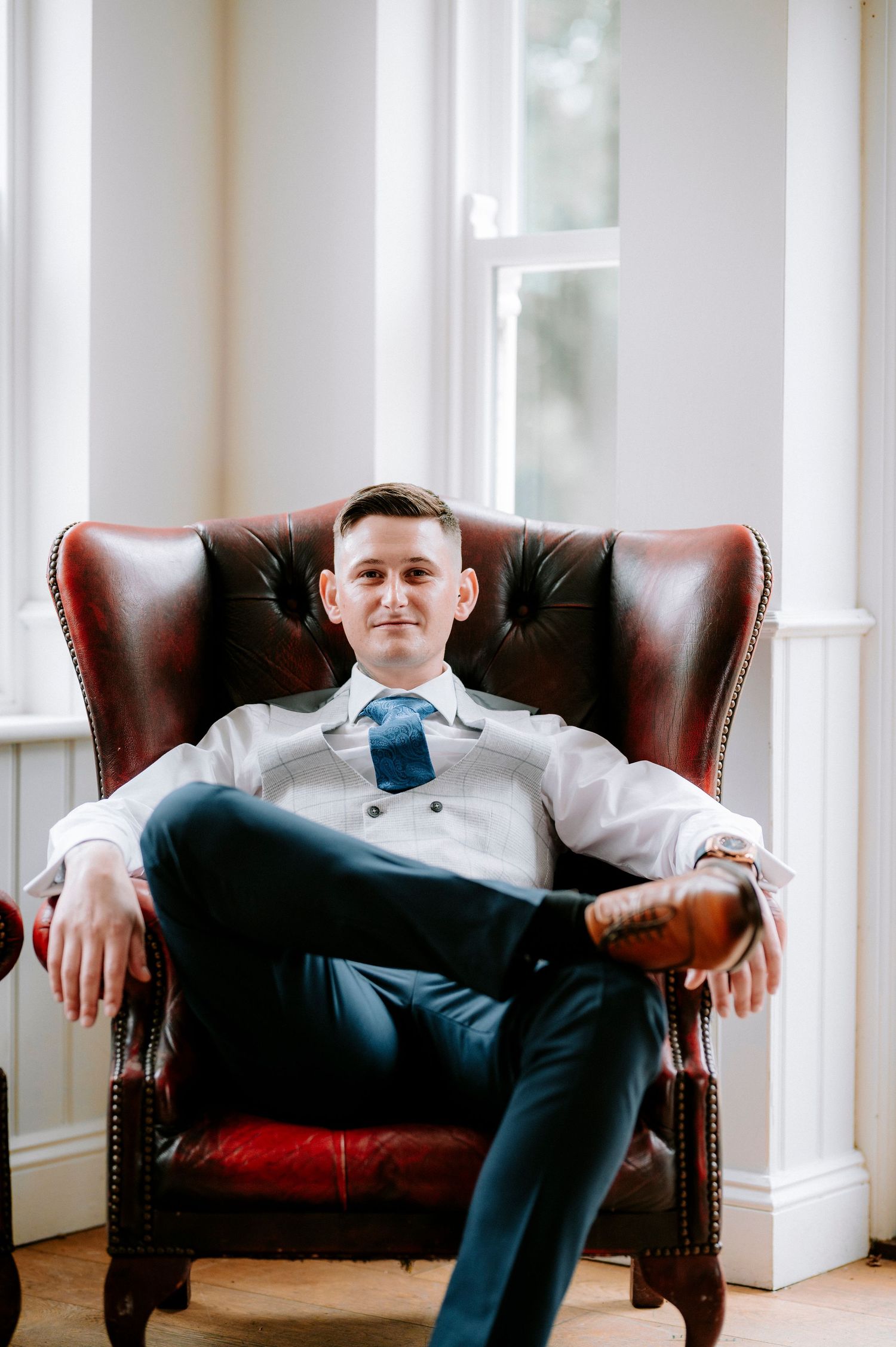 A person in formal attire relaxes in a brown leather wingback chair.