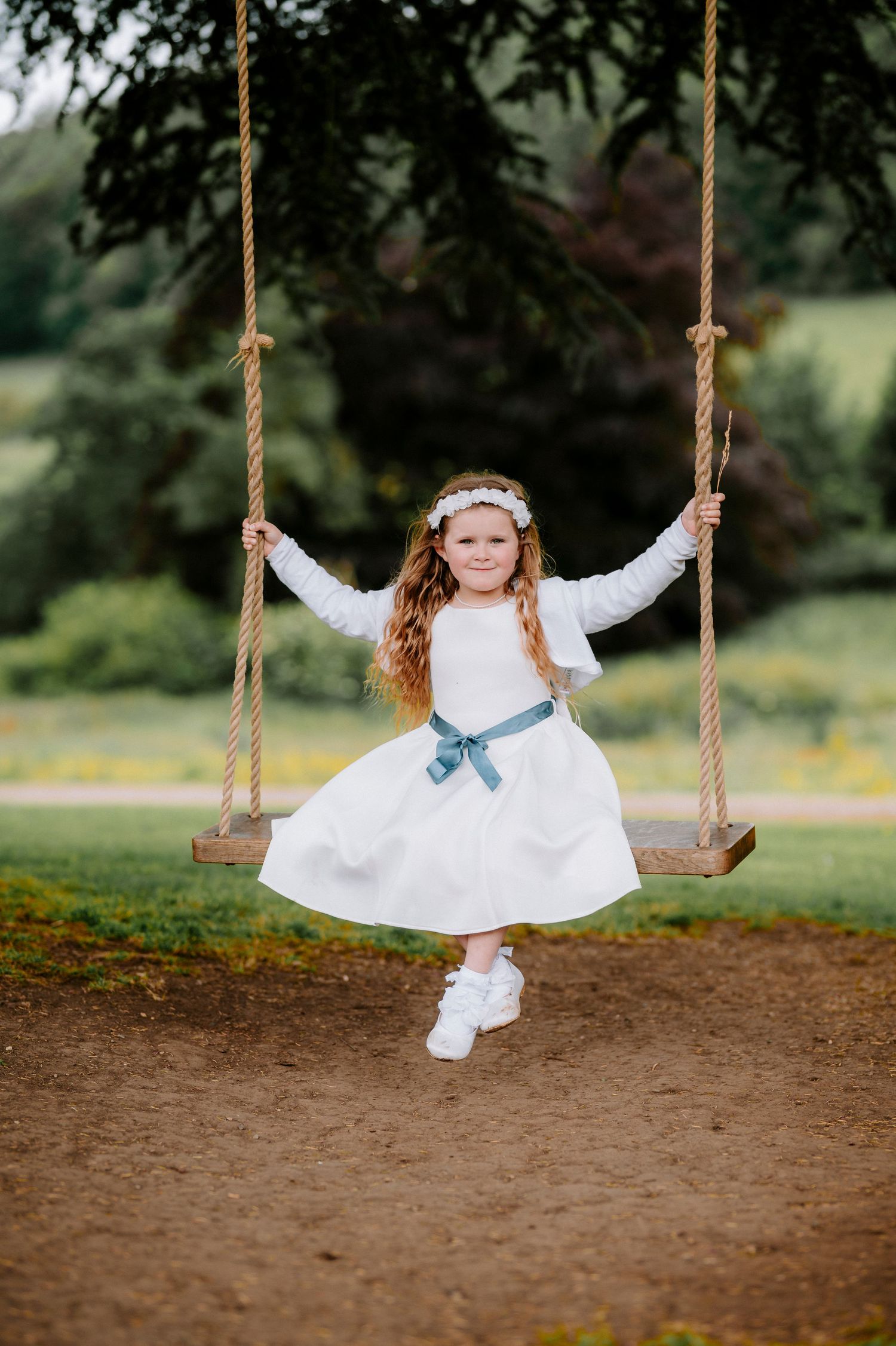 A playful sequence of a person in a white dress swinging on a rope swing in an outdoor garden setting.