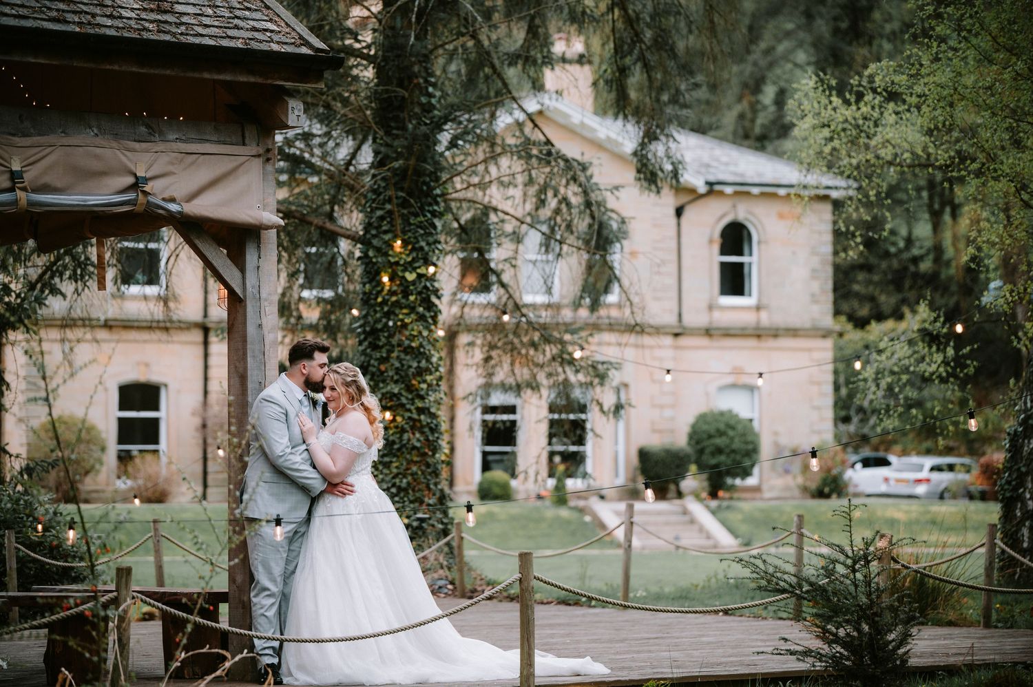 A romantic wedding portrait in front of a historic stone mansion with climbing vines and classic architecture.