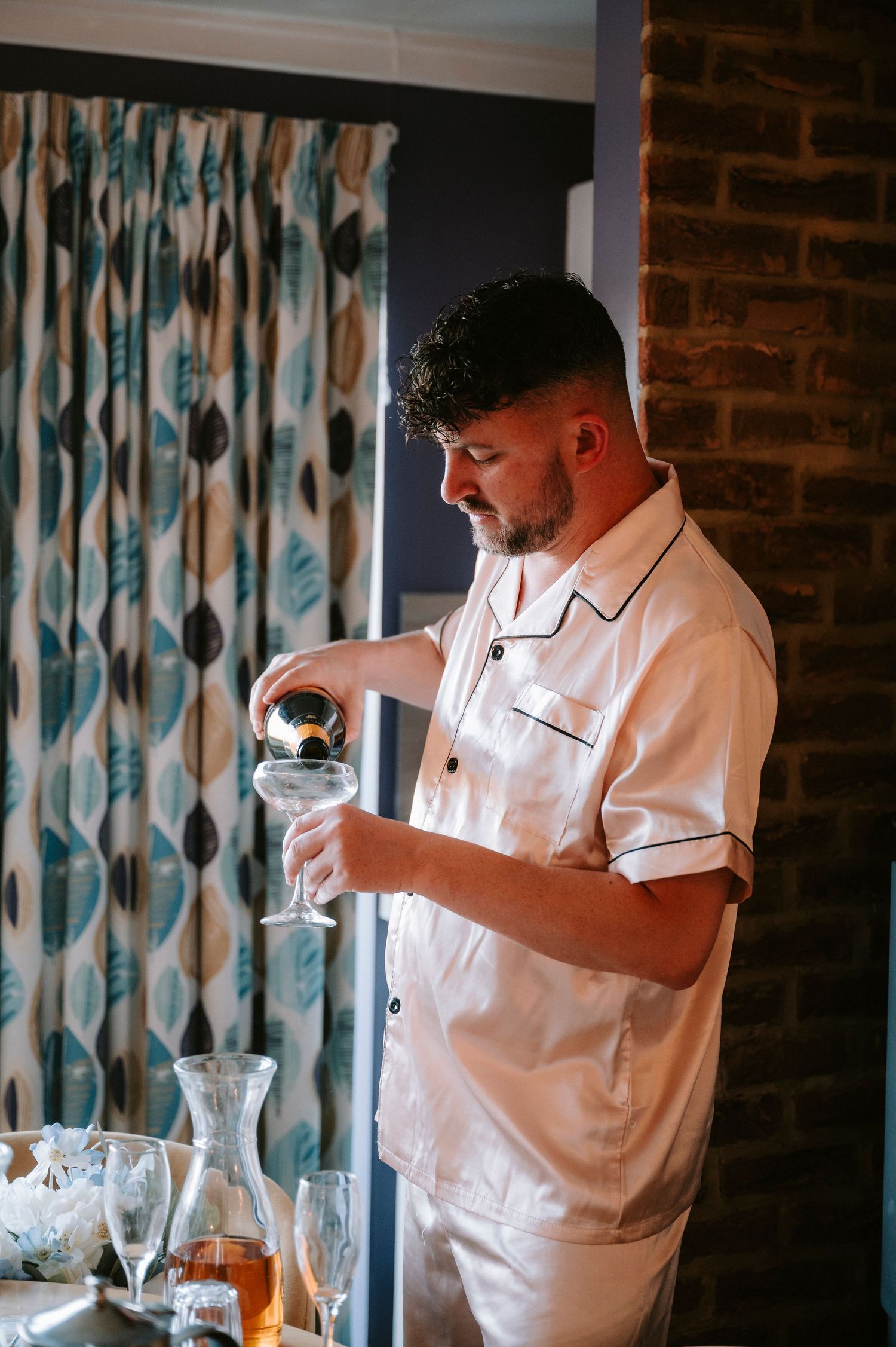 A person in a white shirt pours drinks at a bar counter while examining glassware.