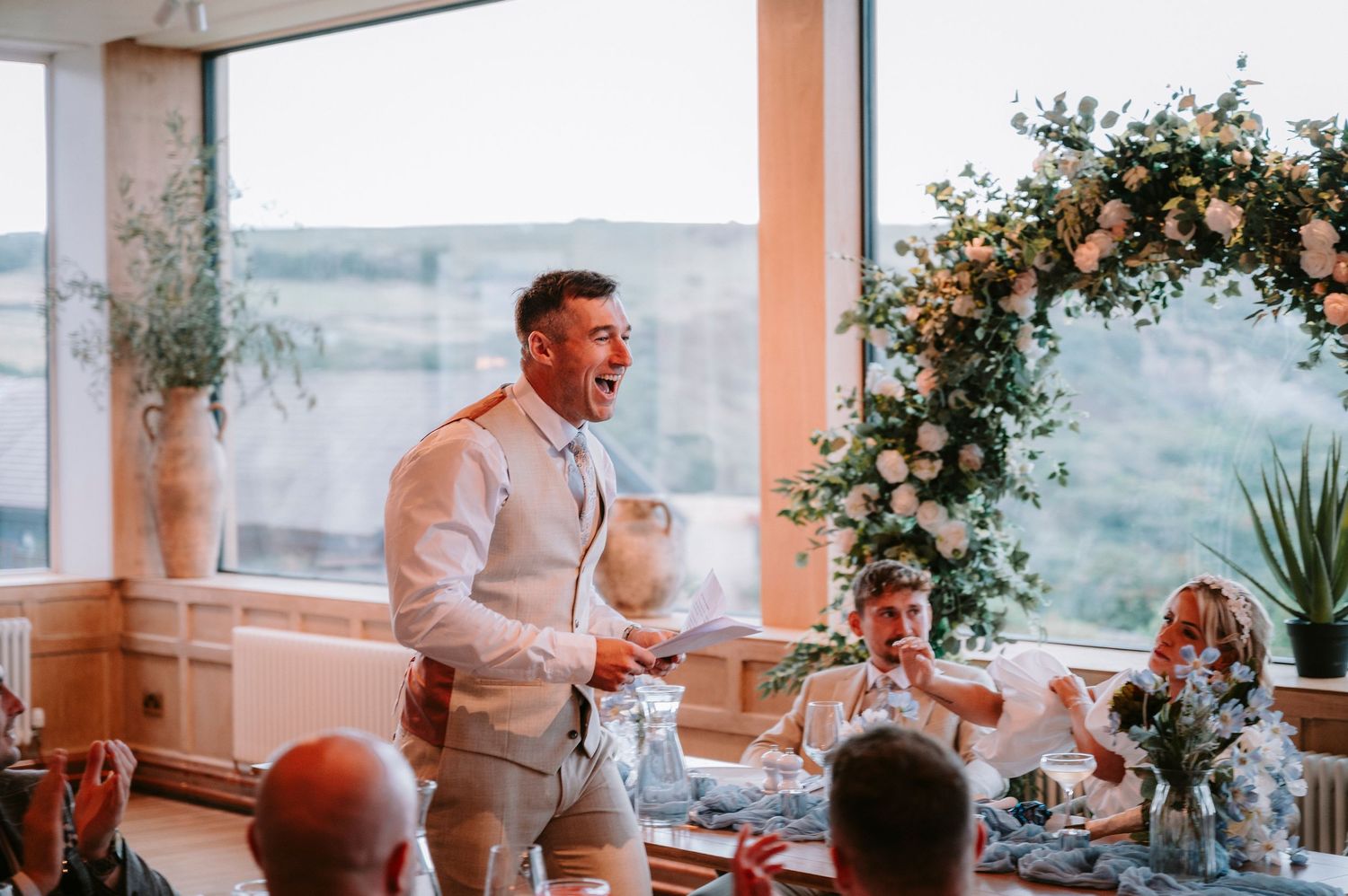 Modern wedding venue with large windows overlooking scenic views and decorated with floral arrangements.