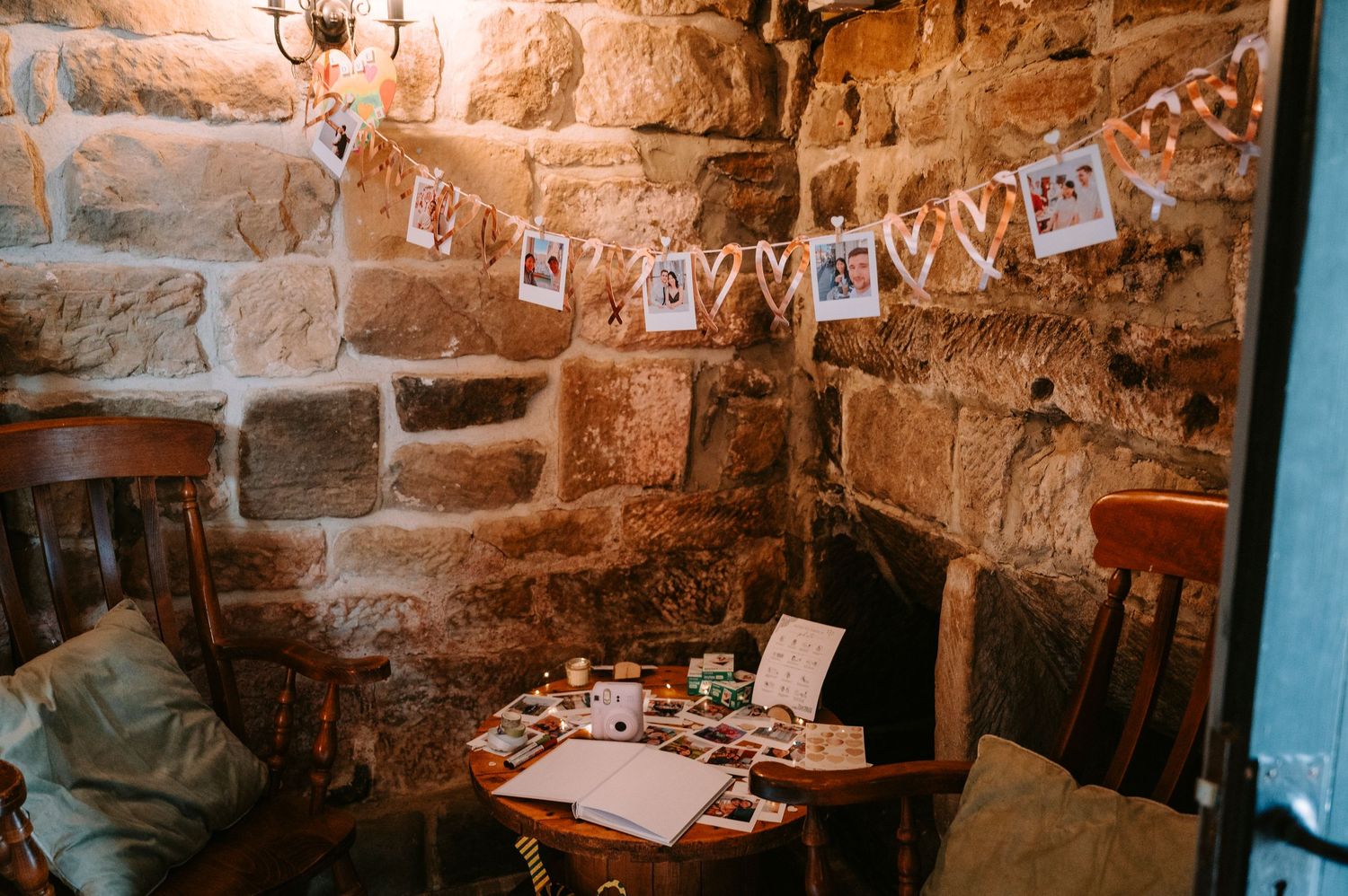 Intimate corner of a stone-walled wedding venue decorated with hanging photo garlands.