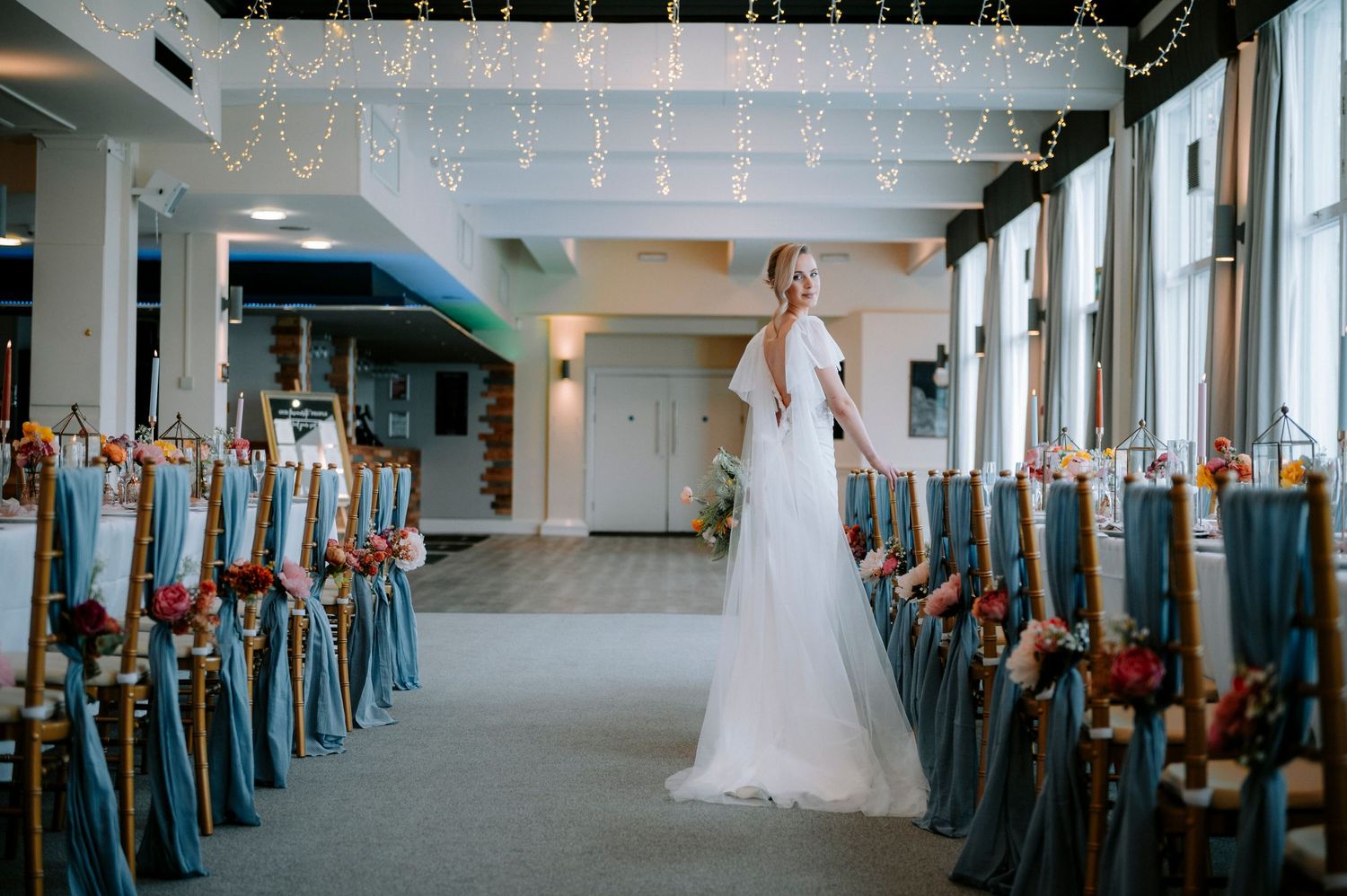 Long wedding venue hall adorned with string lights and teal chair covers.