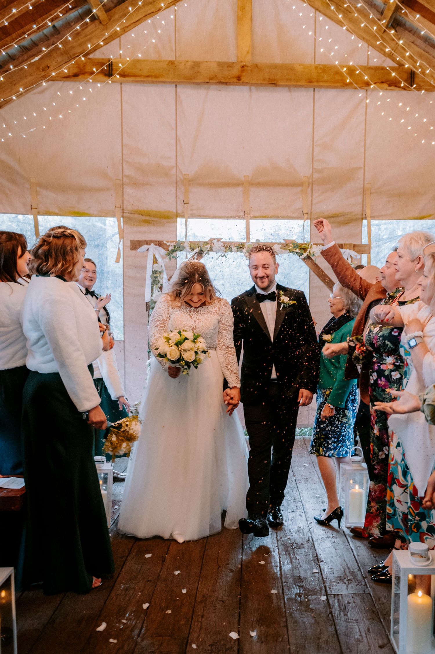 Wedding reception in a rustic barn with string lights and guests celebrating.