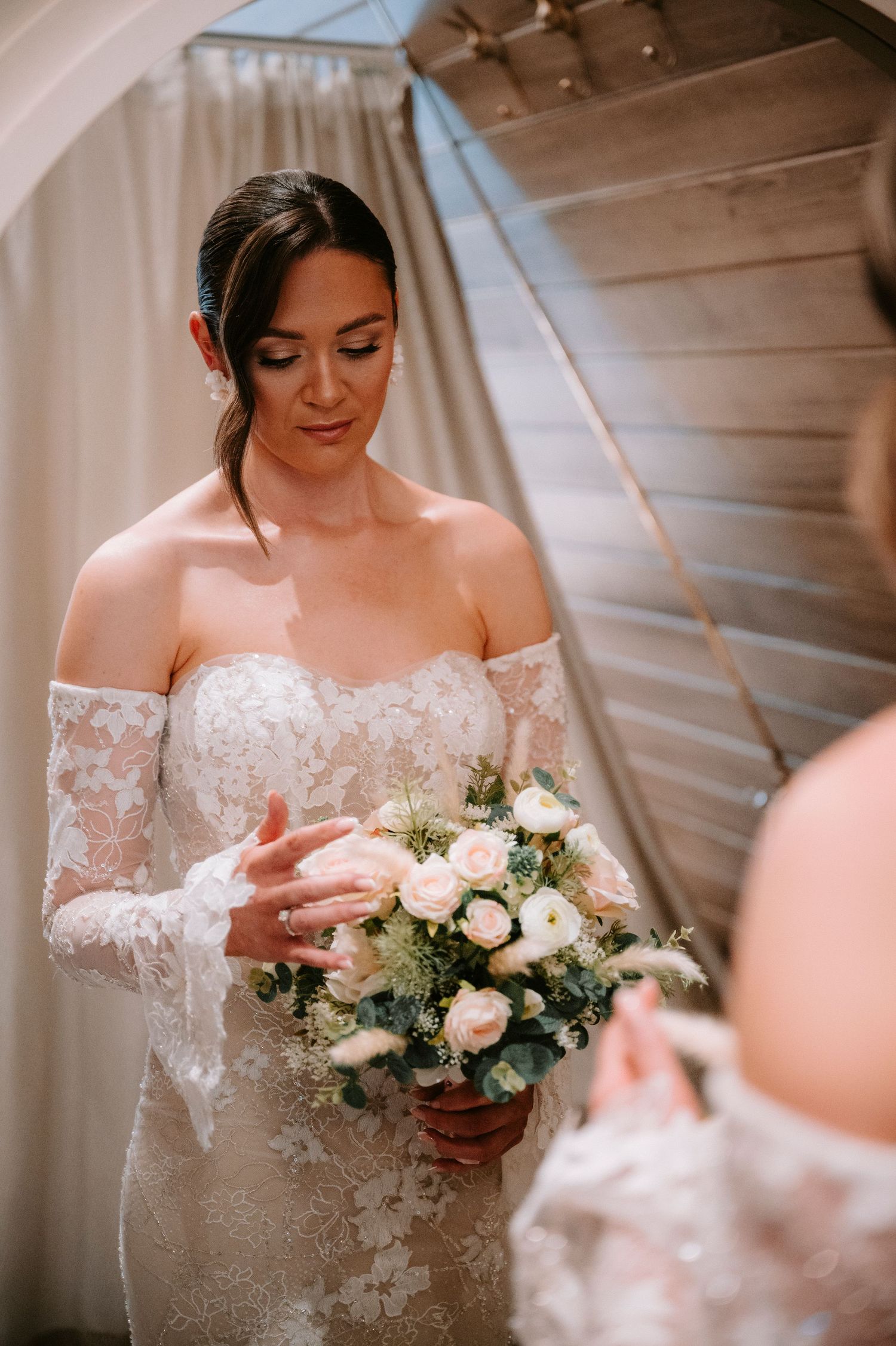 A wedding bouquet of blush roses and white flowers held by a bride in a lace off-shoulder gown.