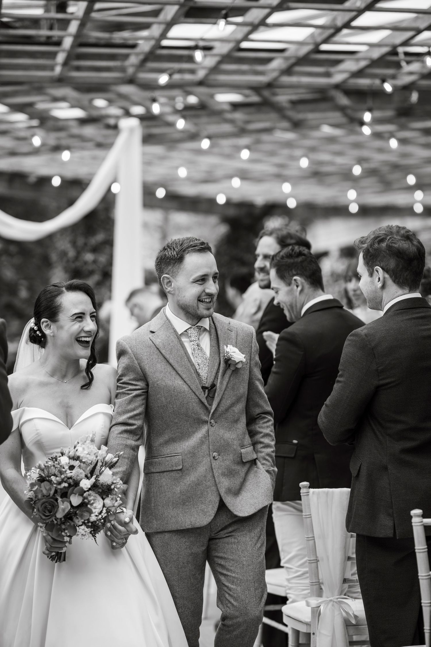 Wedding celebration with laughter under pergola with string lights.