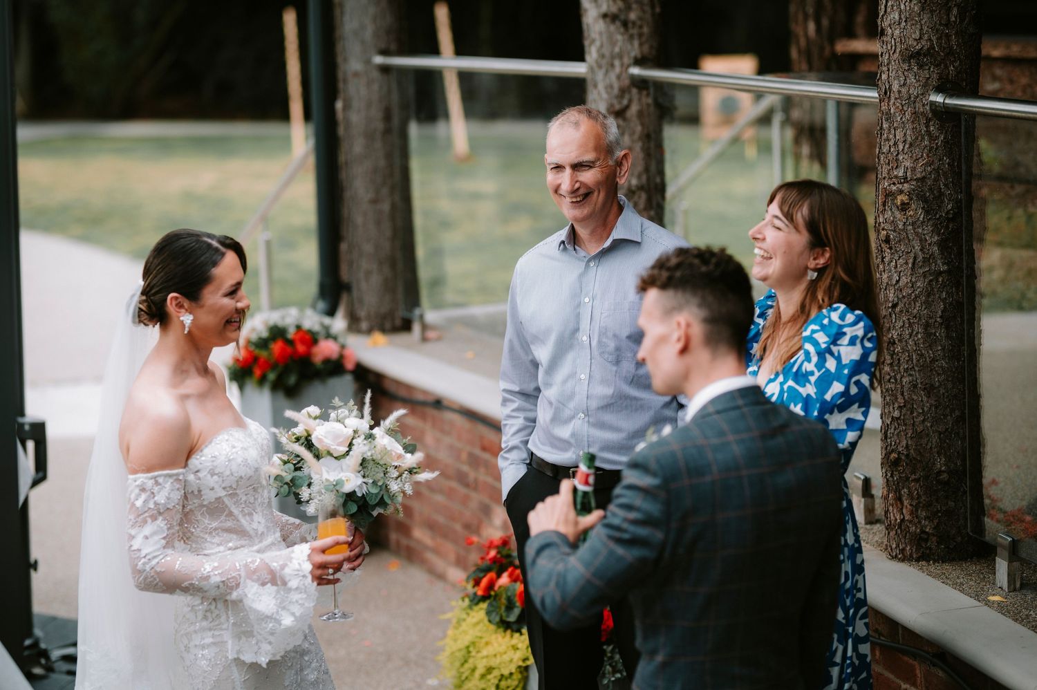 Wedding party gathered outdoors with bride holding bouquet among pine trees.