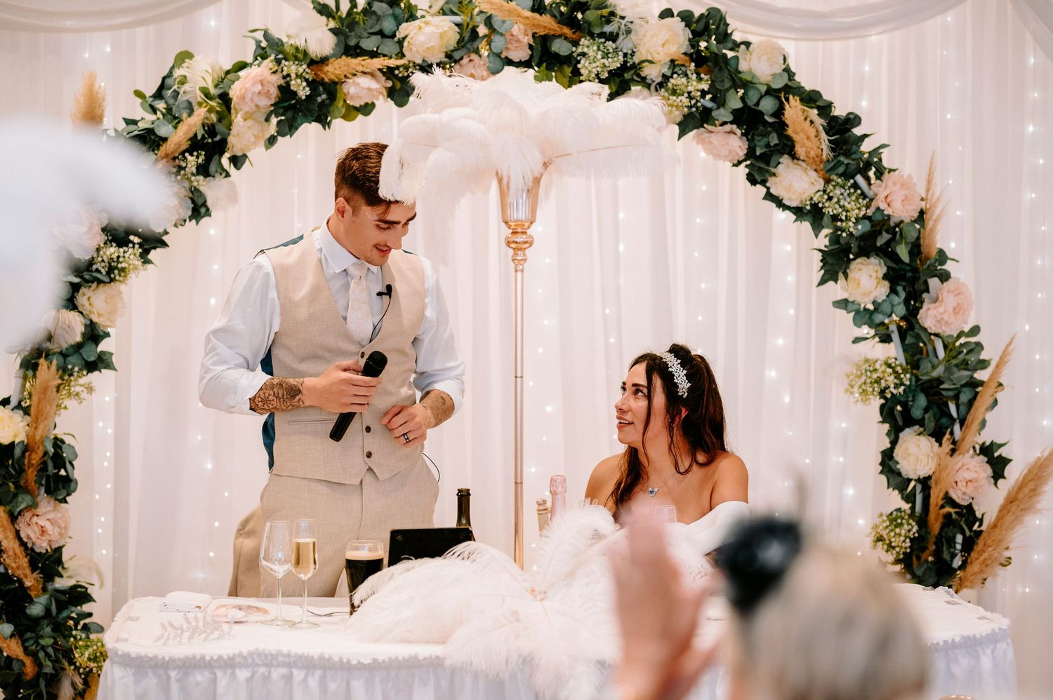A wedding reception setup with a floral arch and white draping decorations.
