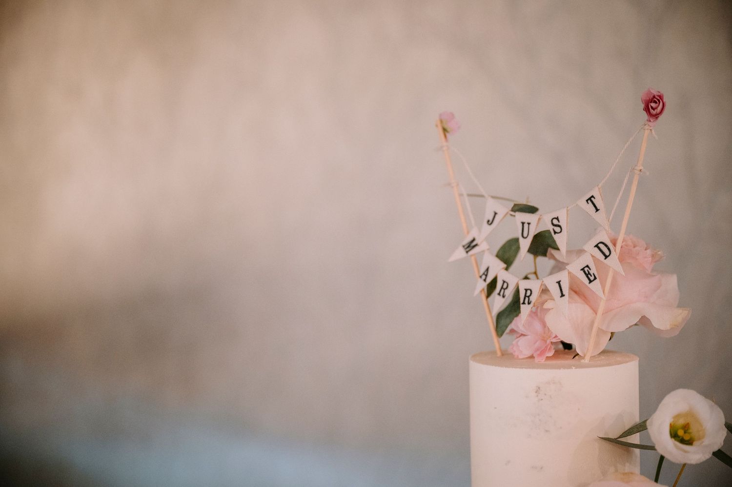Minimalist wedding cake topper with pink accents and eucalyptus leaves.
