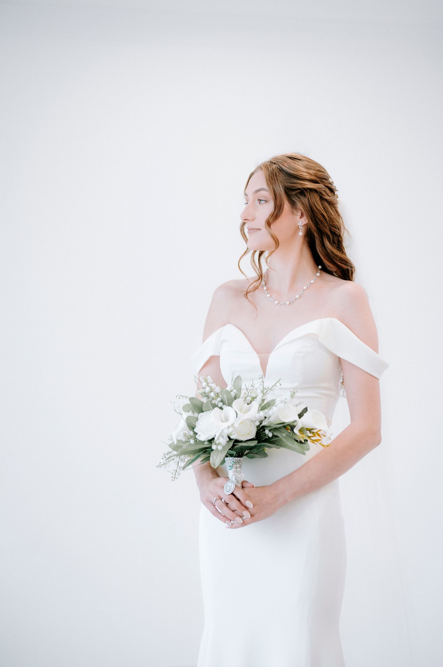 Bride in white off-shoulder gown holding white and green bouquet.