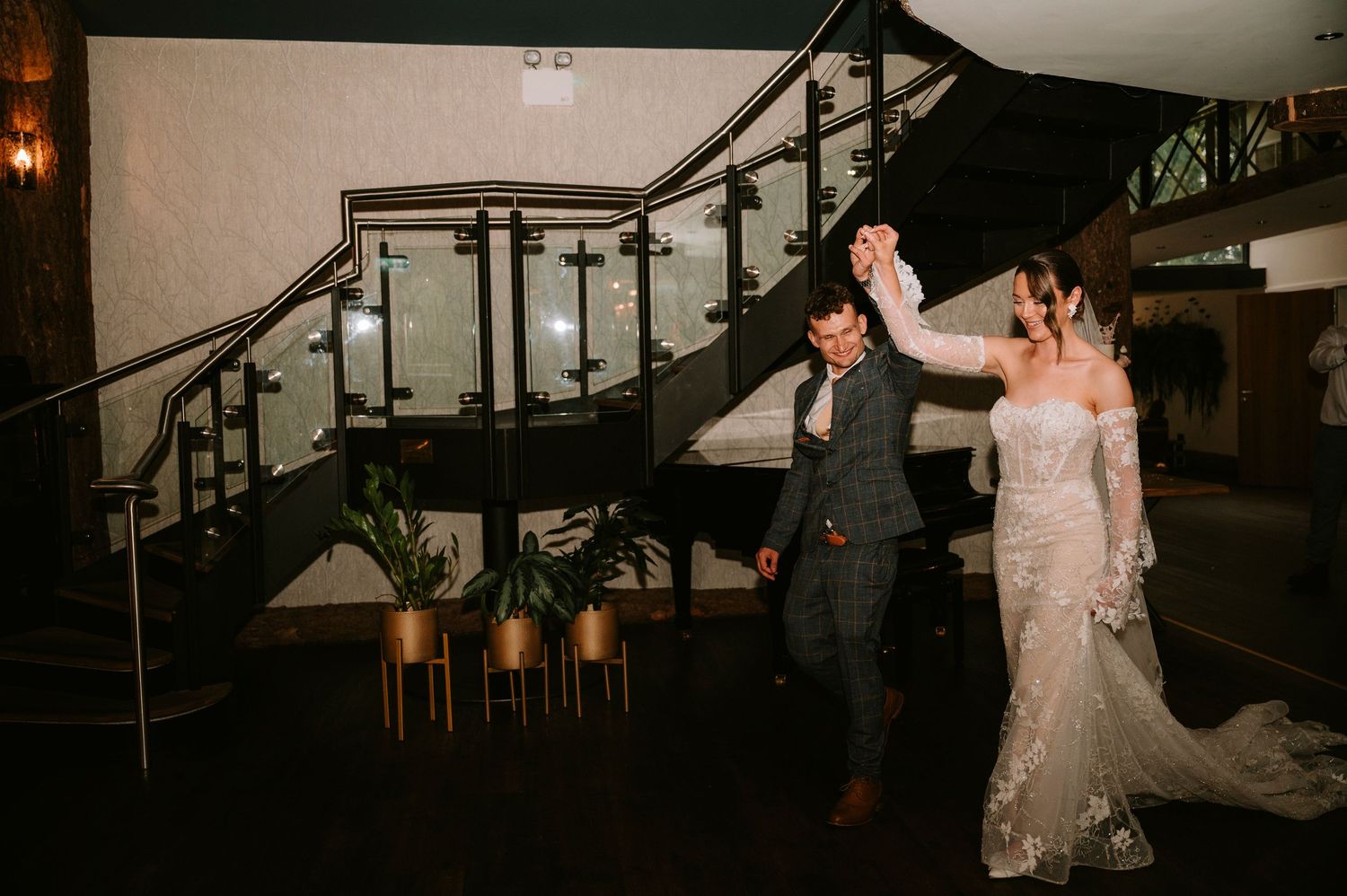 A romantic first dance moment captured in a venue with elegant staircase and warm lighting.