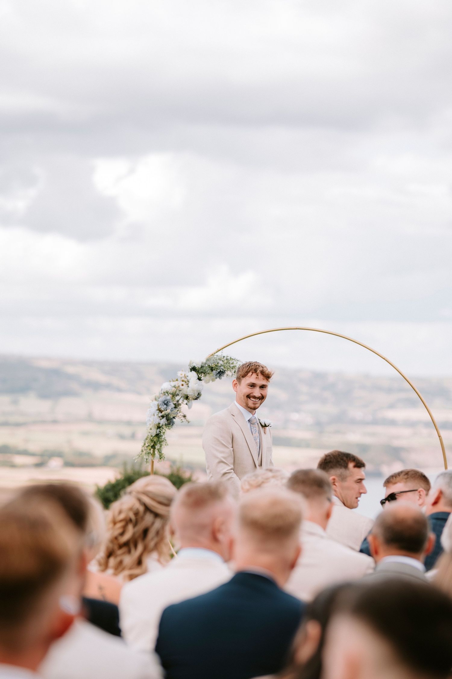 Wedding ceremony taking place outdoors under a circular floral arch with mountain views in the background.