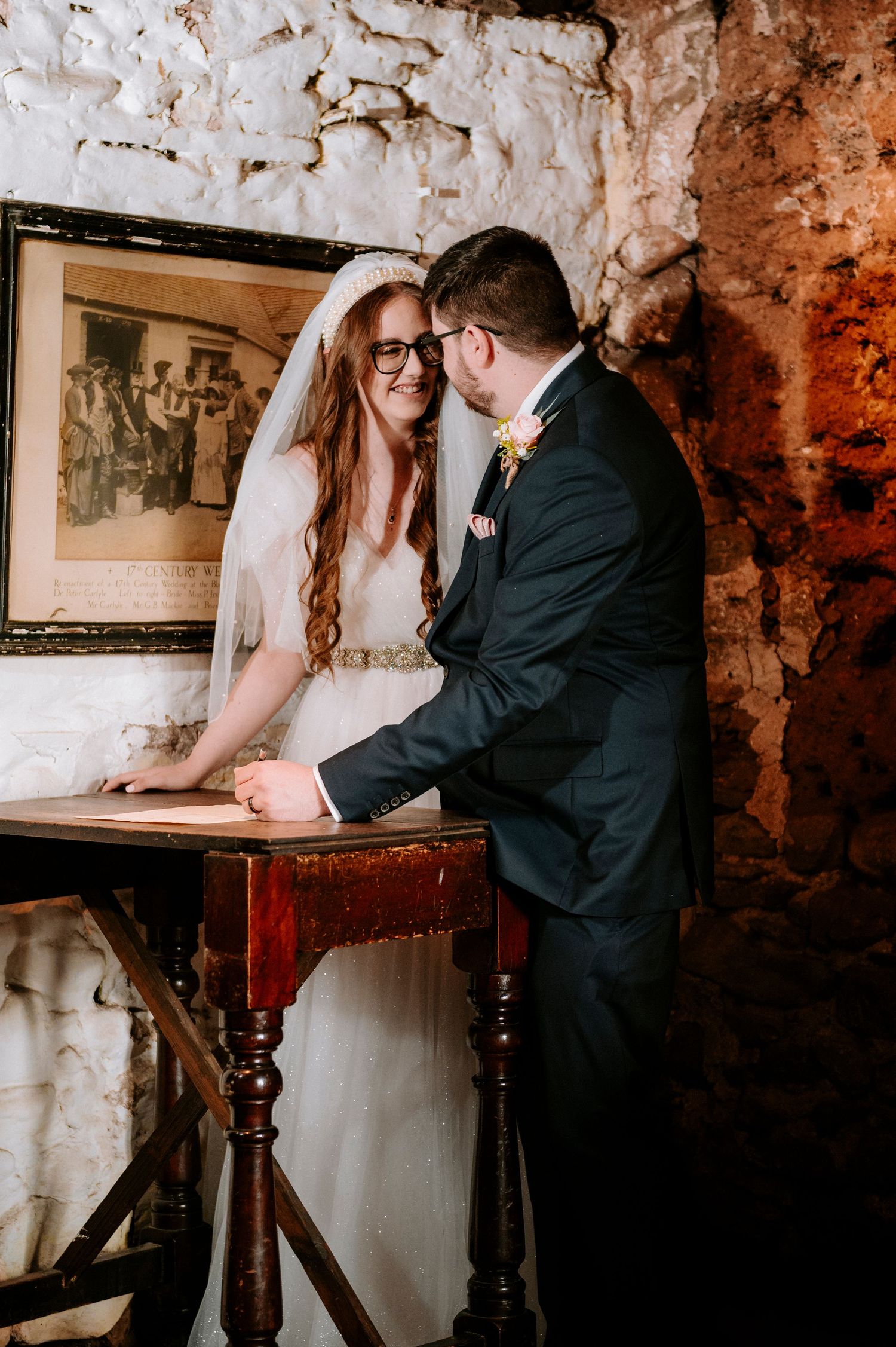 A romantic moment between newlyweds in a rustic stone-walled room with an antique table.
