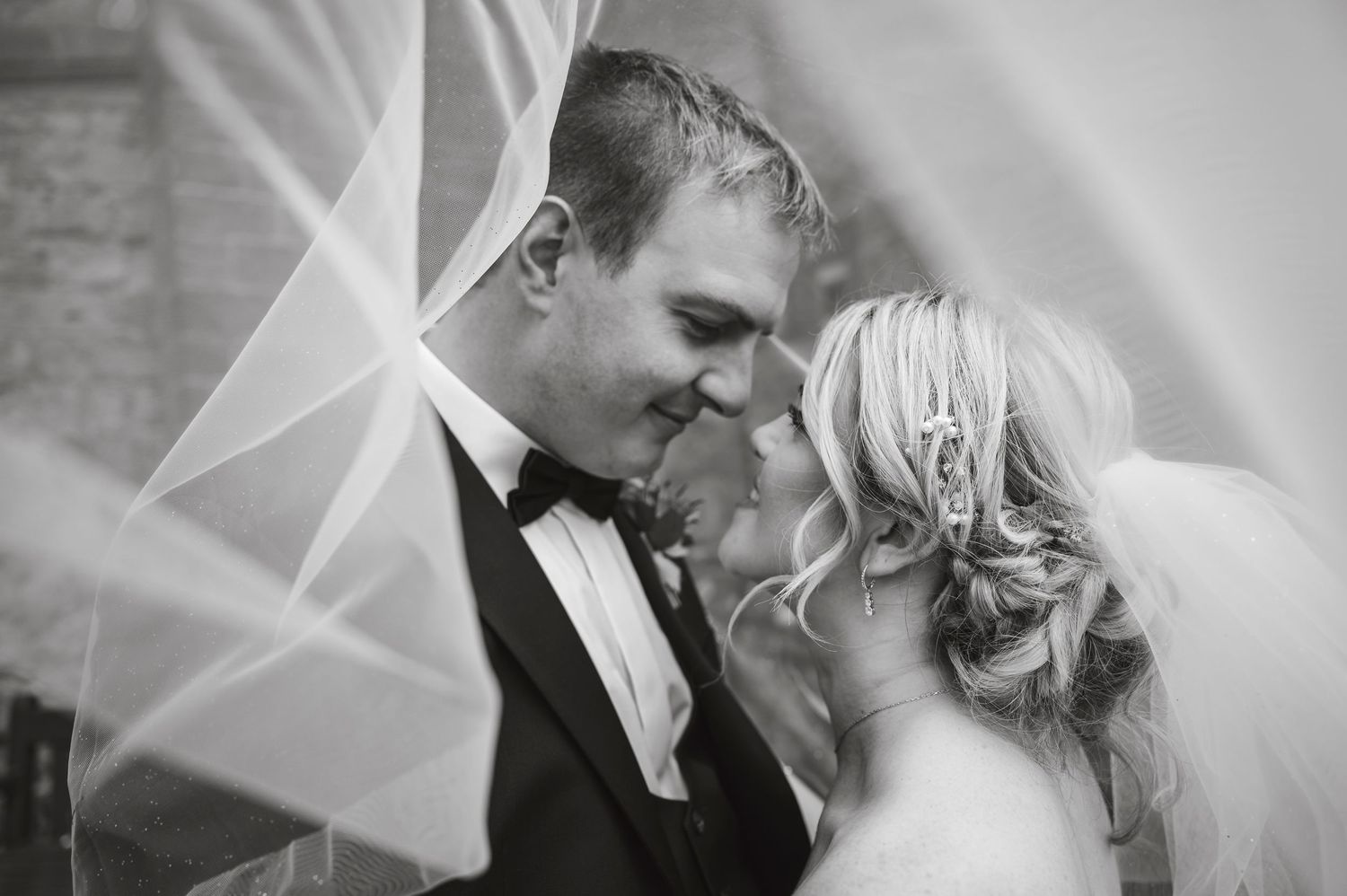 Intimate black and white wedding portrait with flowing veil detail.