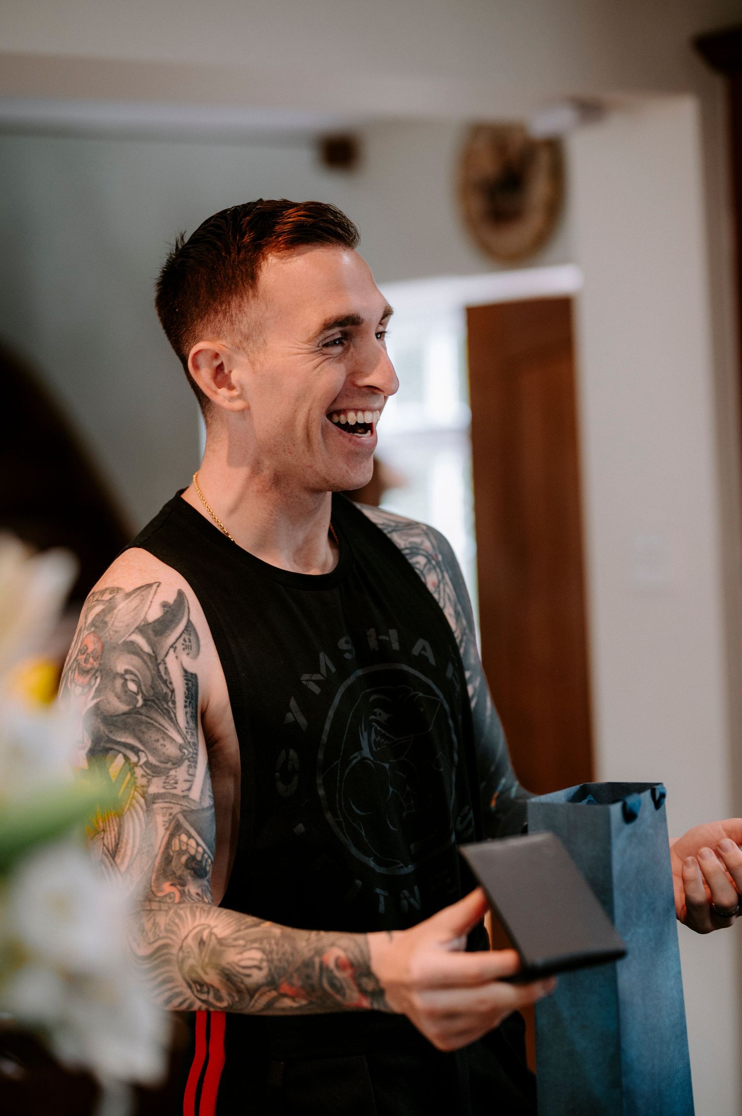 Person in black t-shirt with tattoos reading from paper with joyful expression.