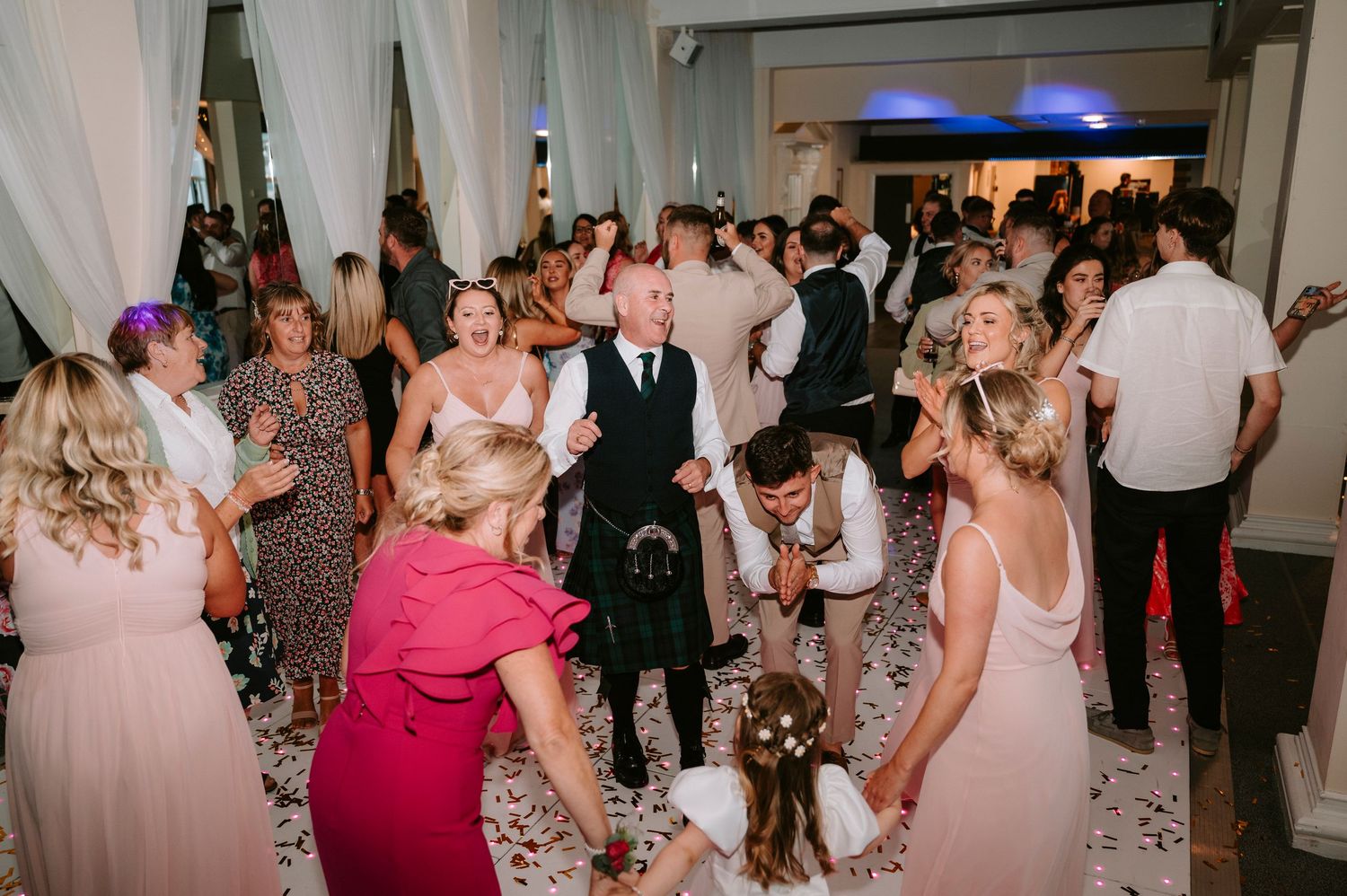 Wedding guests dancing and celebrating on the reception dance floor.