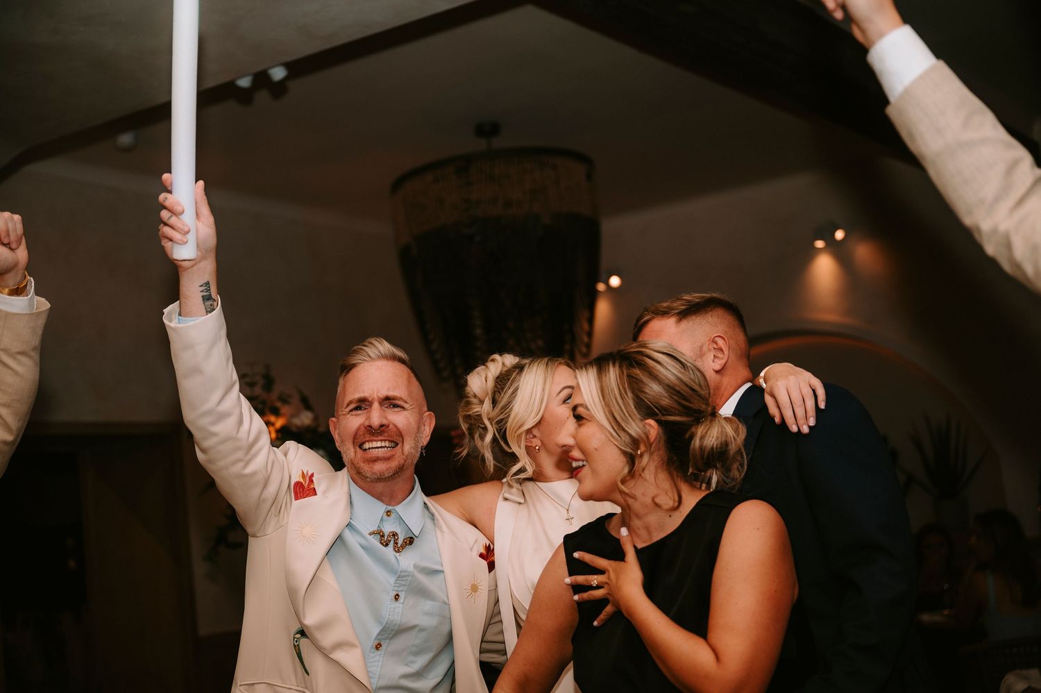 People celebrating and dancing together at a lively wedding reception with raised arms and joyful expressions.