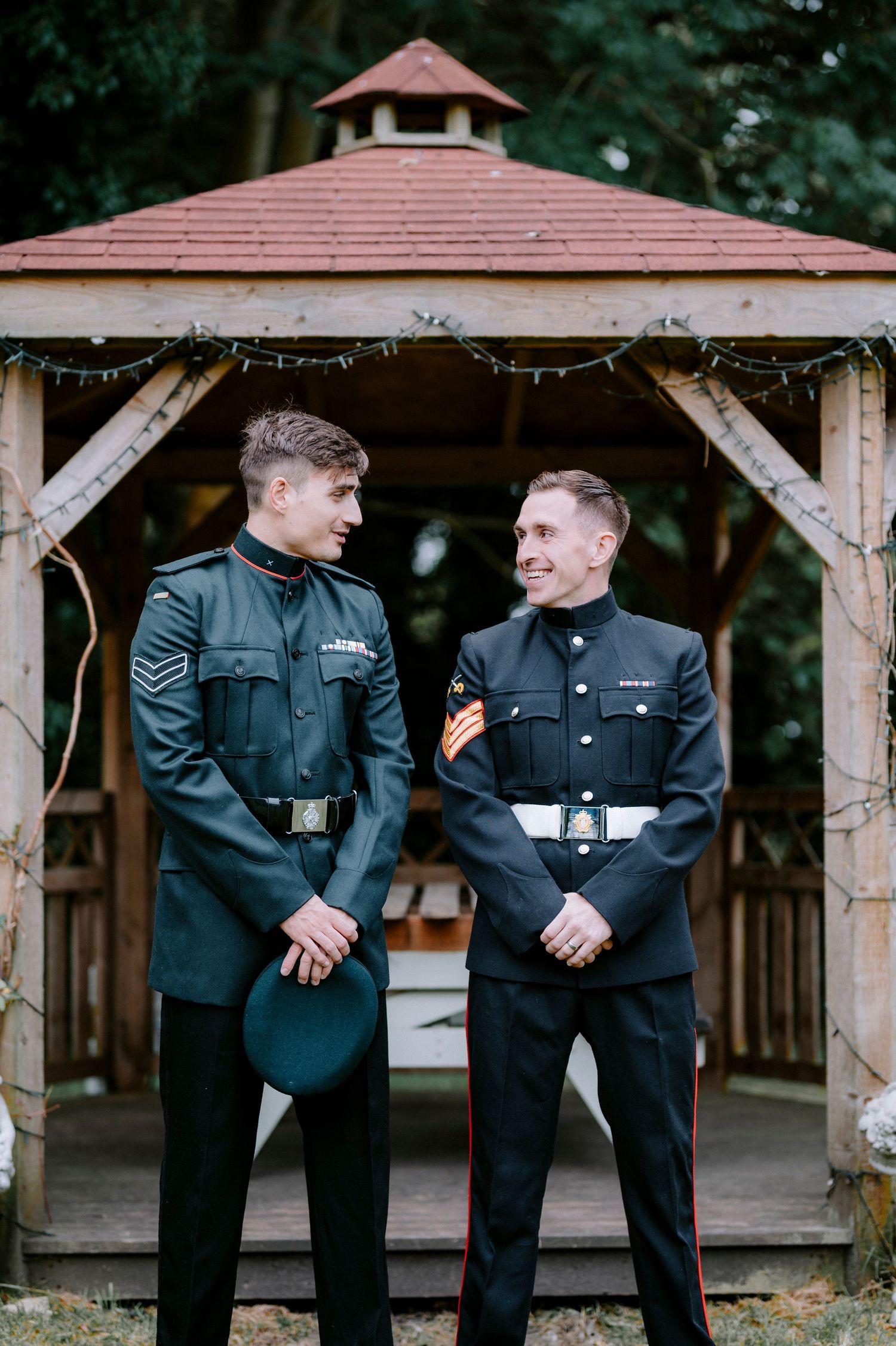 Wedding party members in dark suits standing under wooden gazebo outdoors.