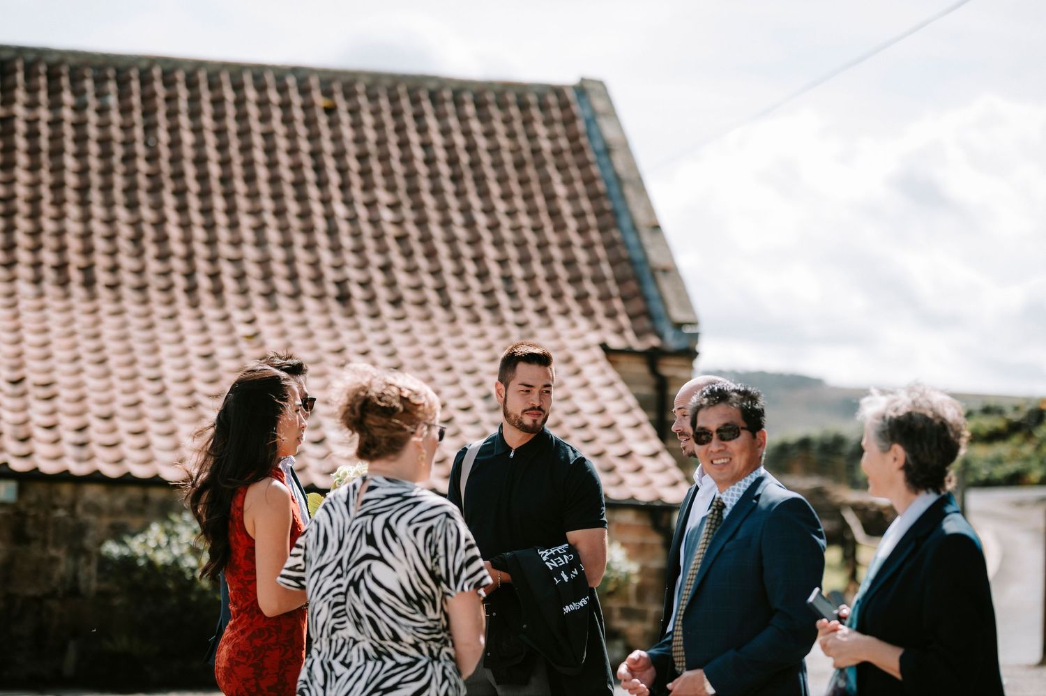Wedding guests mingle outside historic brick building with terra cotta roof.