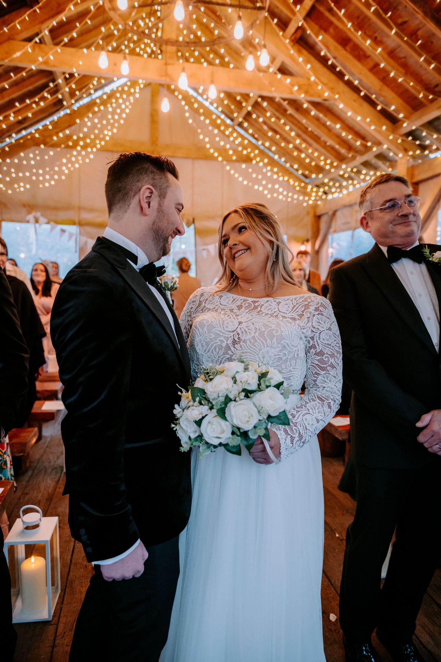A tender ceremony moment in a barn venue illuminated by romantic string lights.