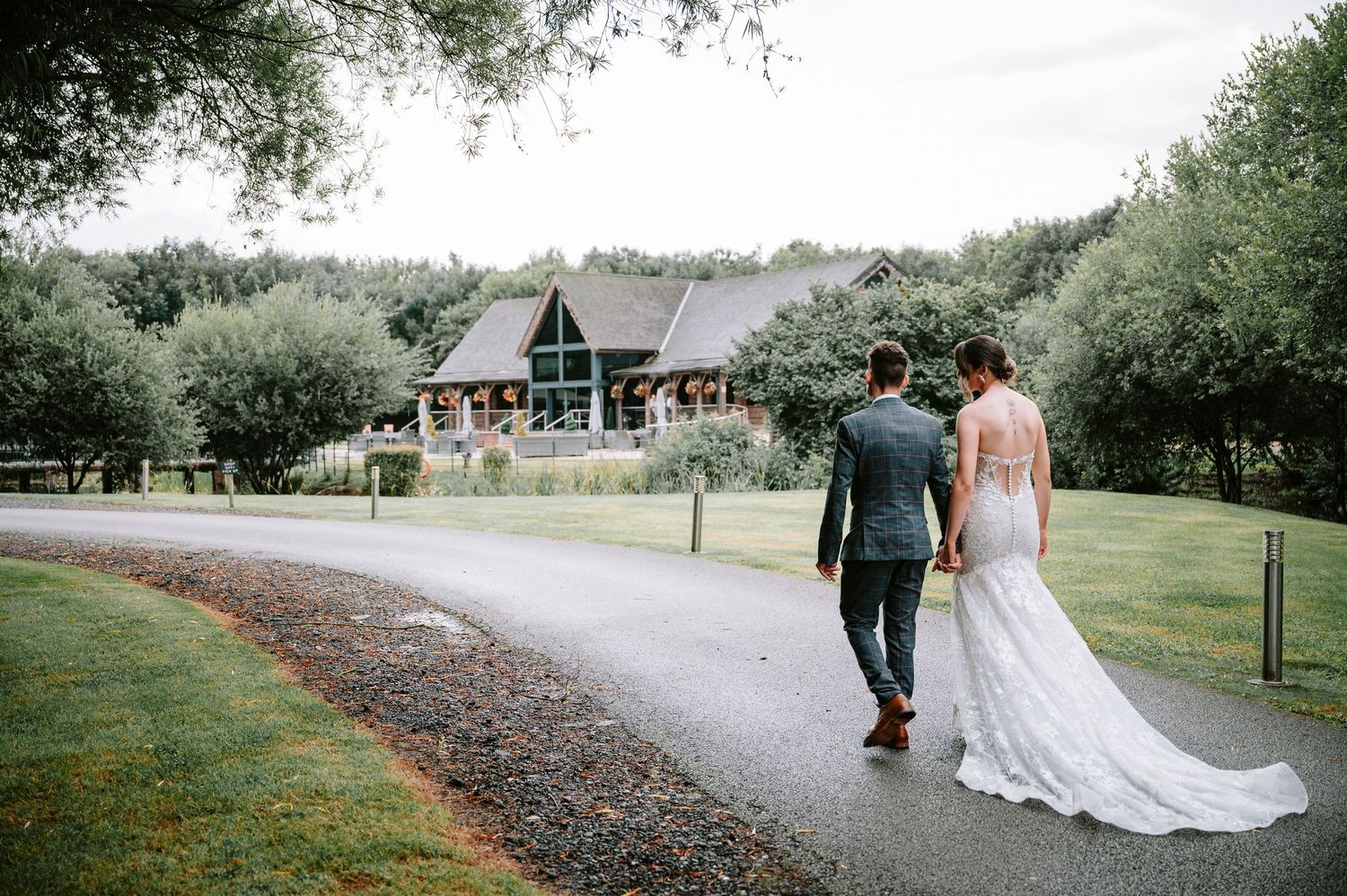 Bride and groom walking hand in hand down a countryside path towards their wedding venue.