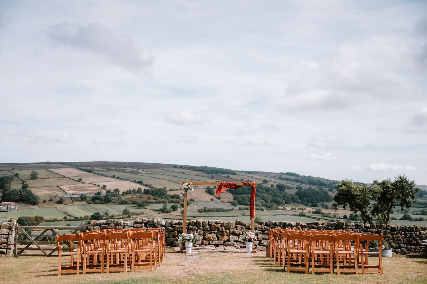 Outdoor wedding ceremony setup with wooden chairs overlooking a scenic countryside landscape.