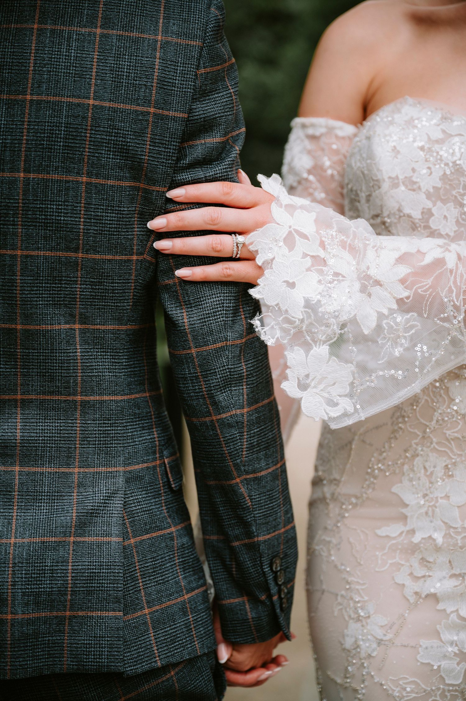Close-up details of a white lace wedding dress and plaid suit jacket.