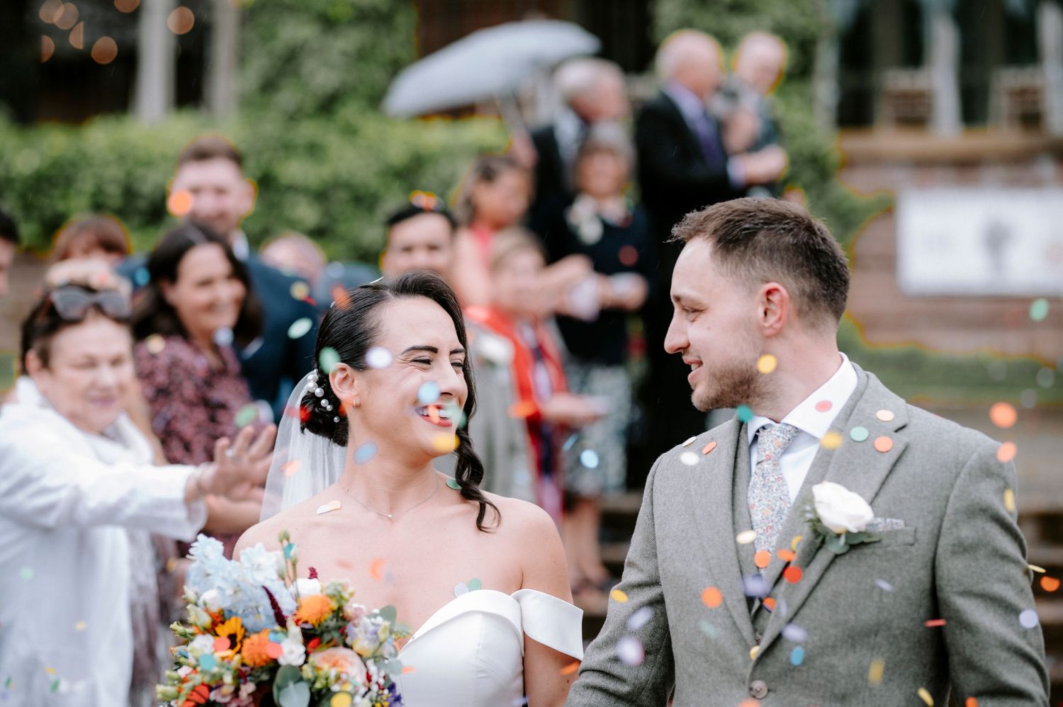 Outdoor wedding party shares joyful moments under wooden pergola.