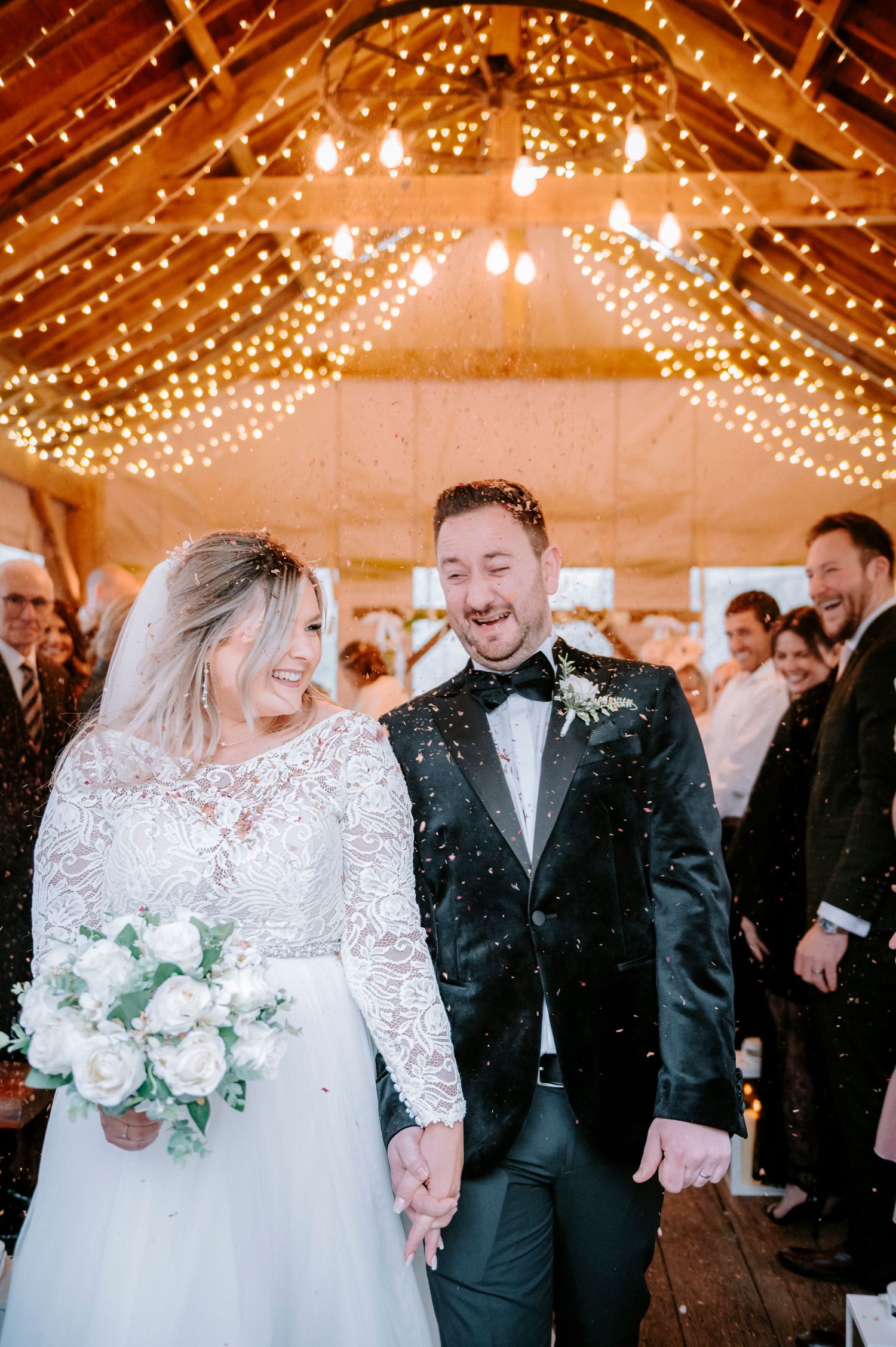 Newlyweds celebrating under twinkling lights in a rustic barn venue with wedding guests.