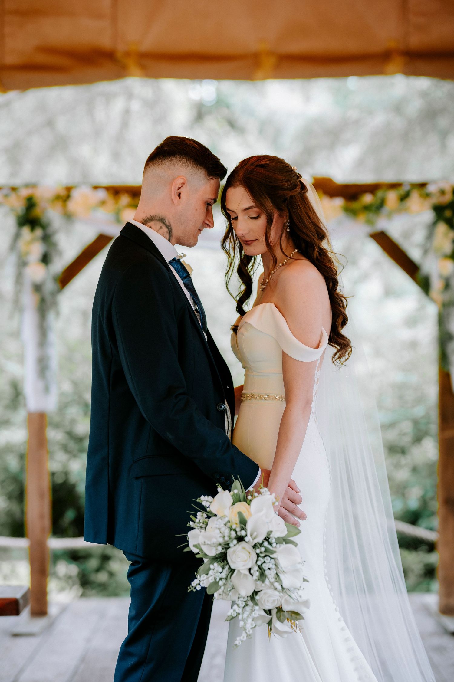 Romantic wedding ceremony moments under a covered outdoor venue with white floral decorations.