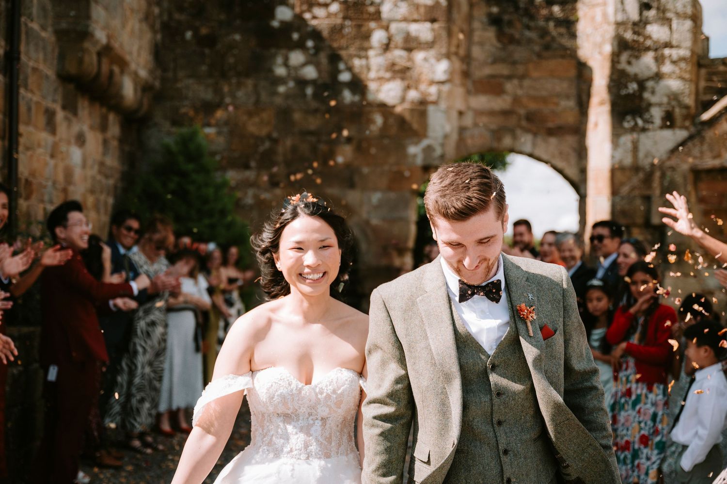 Newlyweds and wedding party celebrate during outdoor reception by stone walls.