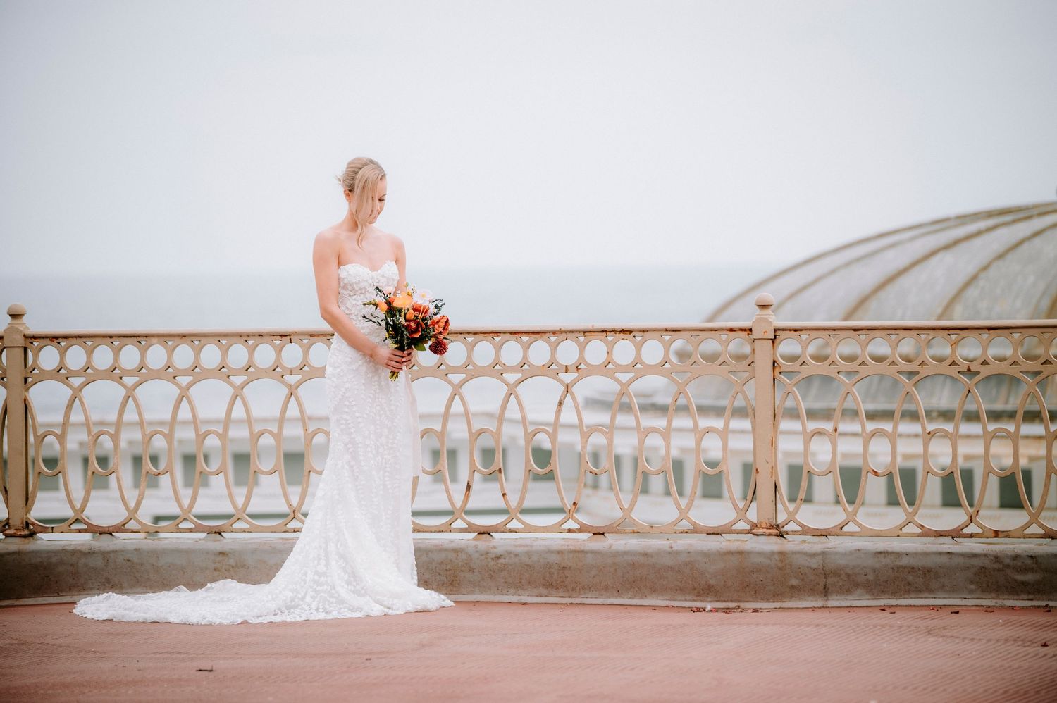 A bride in white stands against an ornate balustrade railing with vintage architectural details.