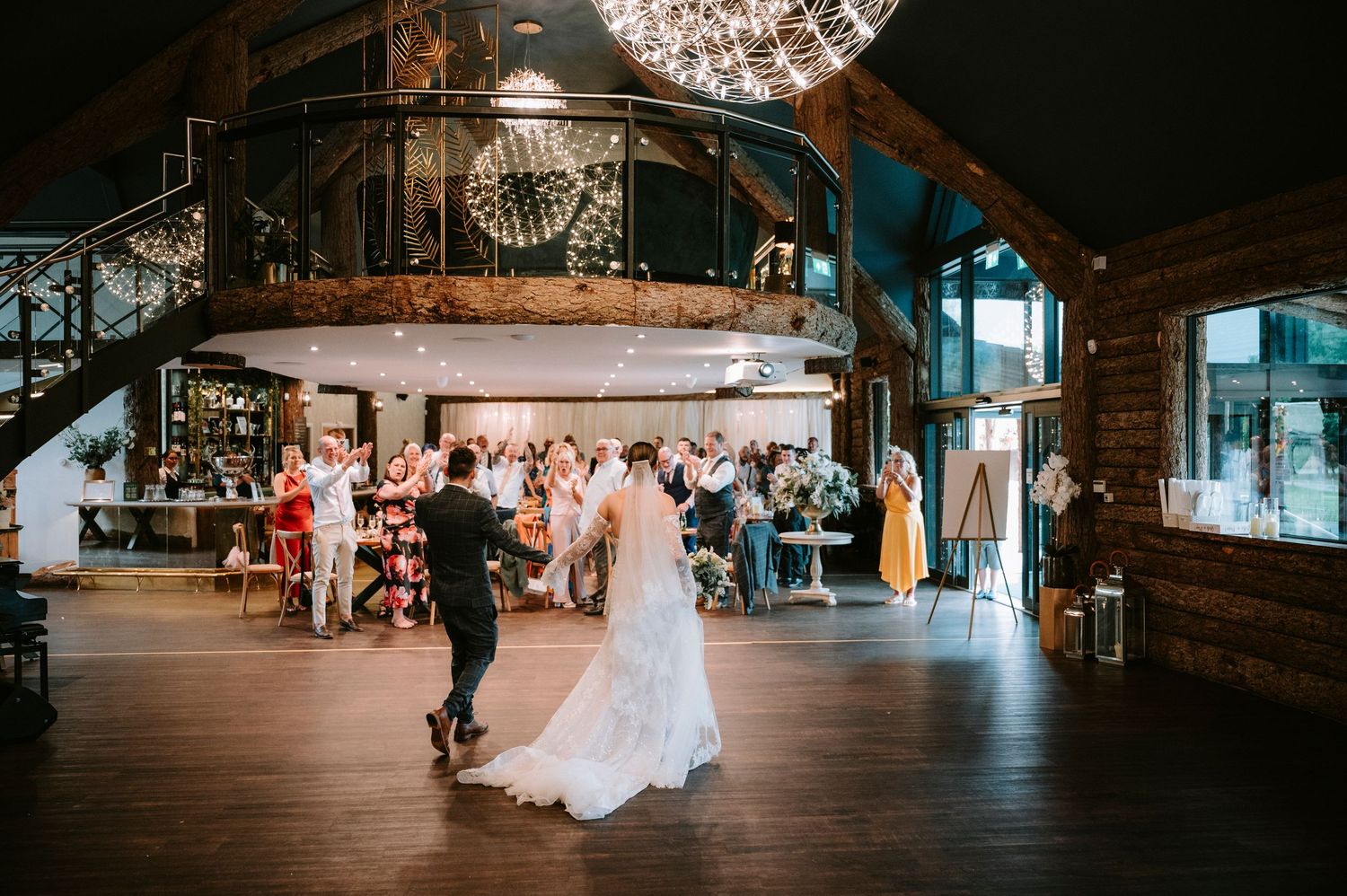Wedding couple dances under sparkling disco ball in elegant industrial venue during first dance celebration.