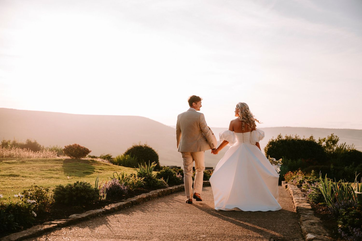 Romantic sunset silhouette of newlyweds walking along a coastal path.