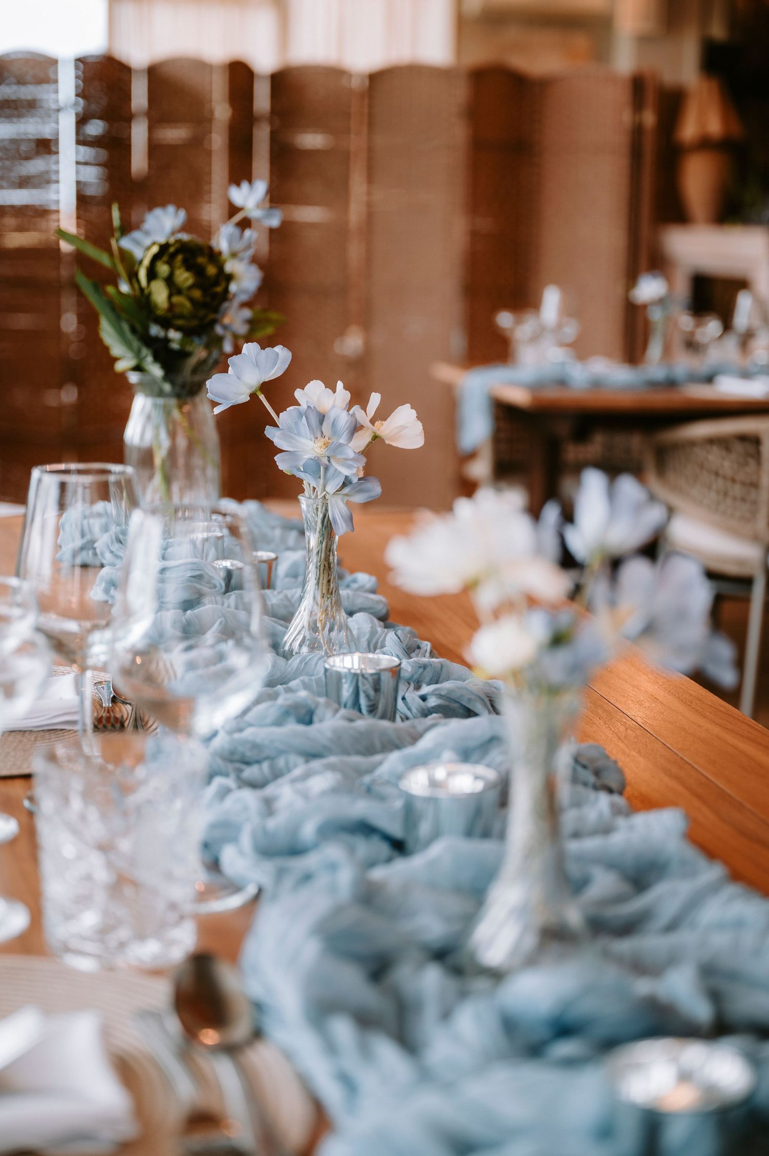 Elegant wedding table setting with blue chiffon runner and delicate floral centerpieces.