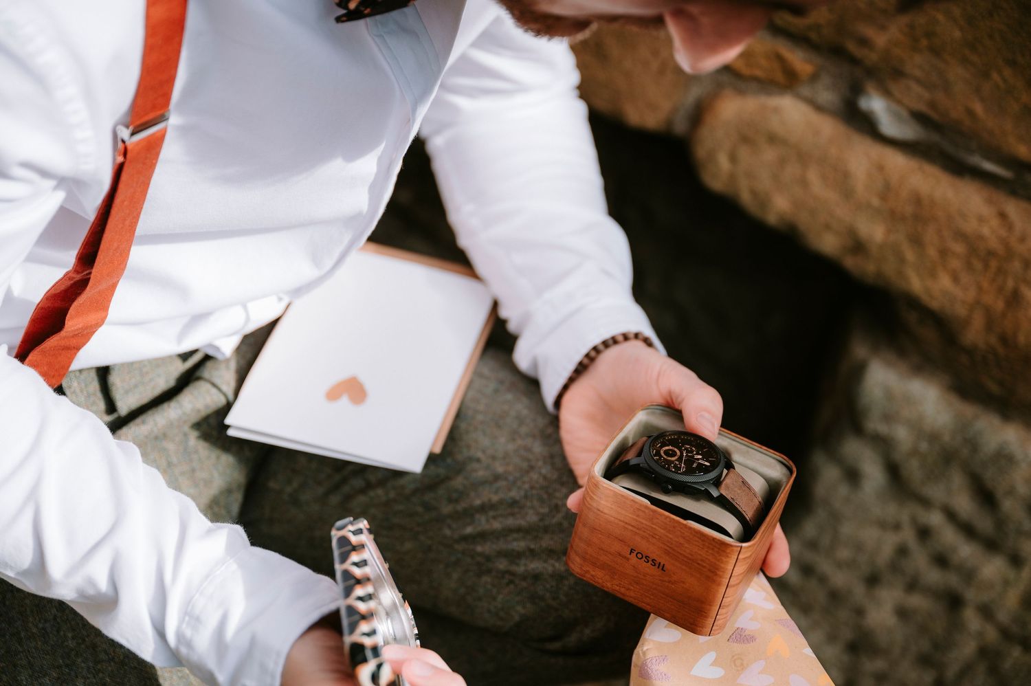 Wedding guests writing messages in a guest book with pens on a rustic wooden surface.