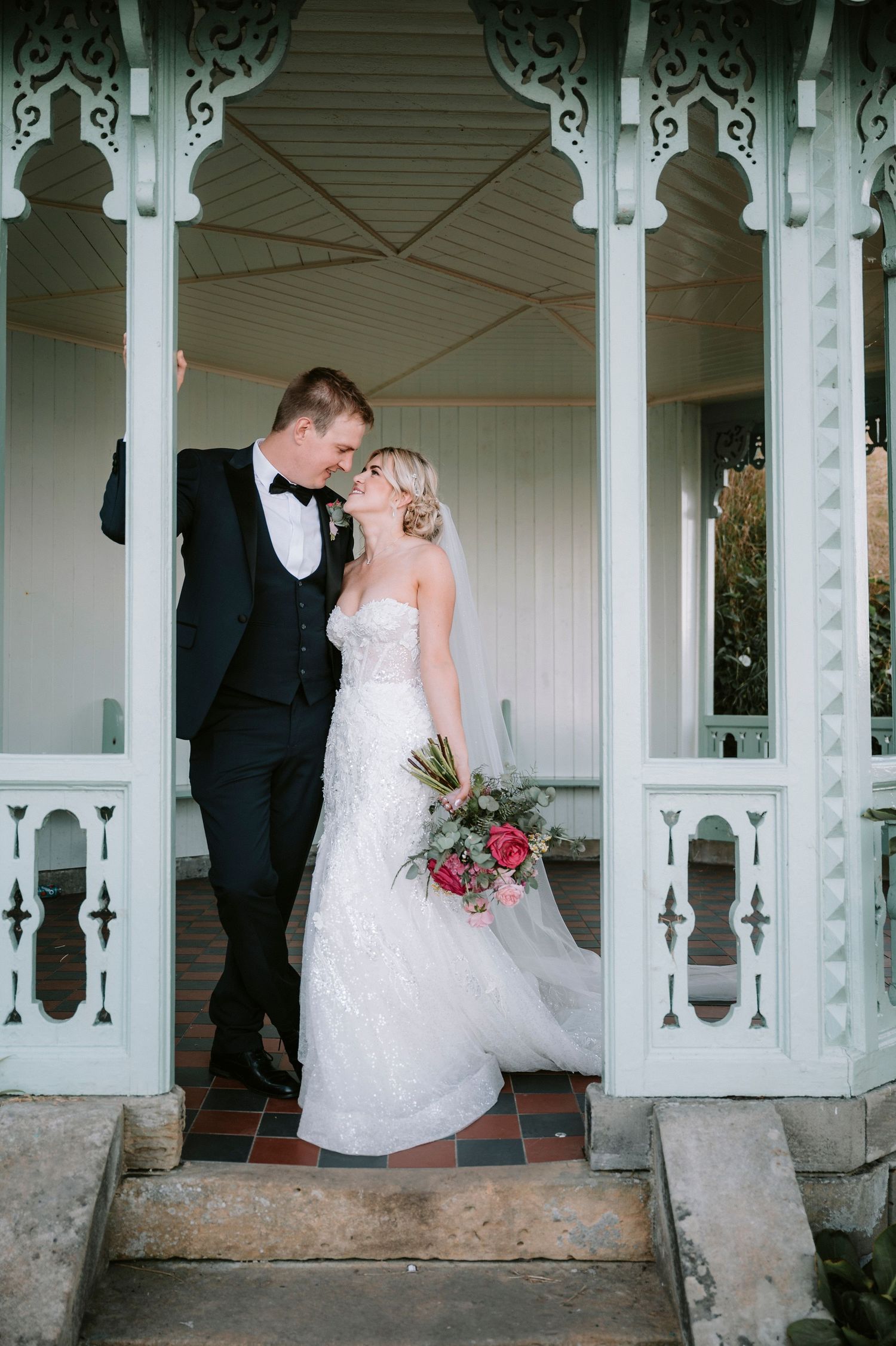 Wedding portraits taken under ornate white Victorian porch columns with decorative details.